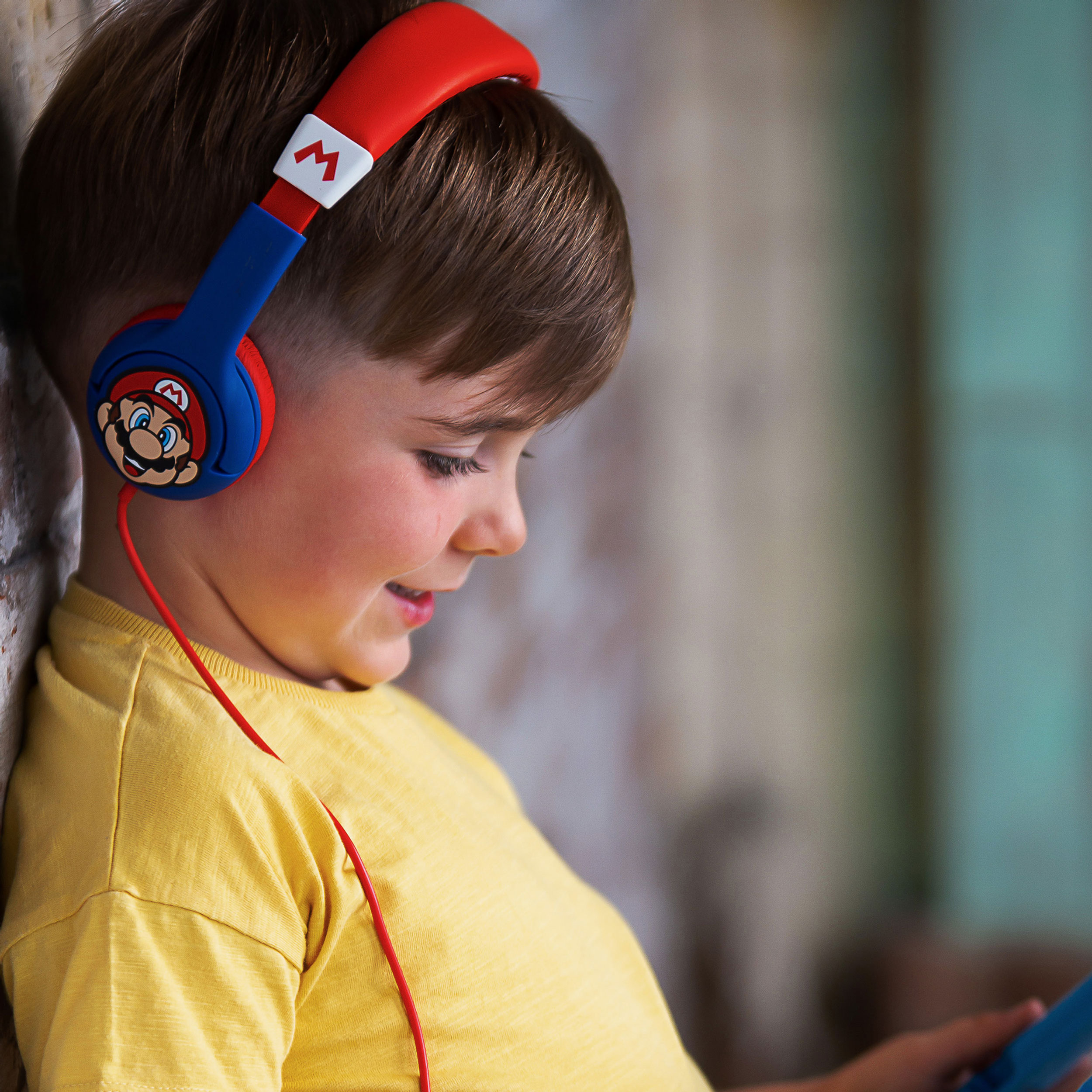 Ragazzo con cuffie a tema Mario, che tiene in mano un tablet, appoggiato a un muro di mattoni.