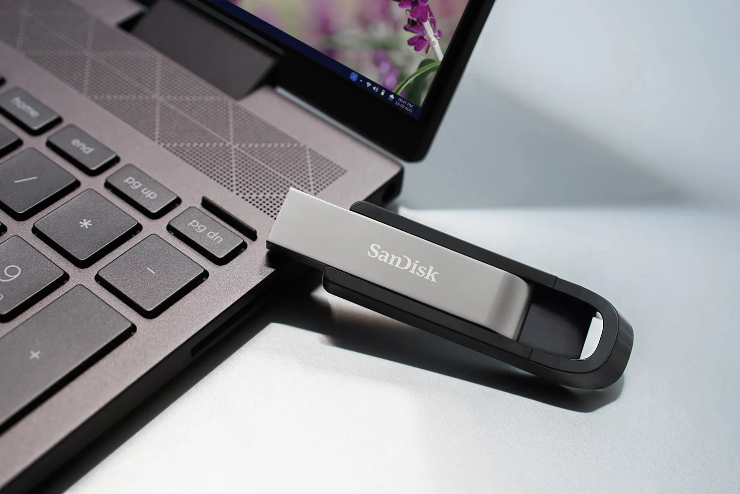 Chiavetta USB SanDisk argentata e nera collegata a un laptop. Sfondo bianco.