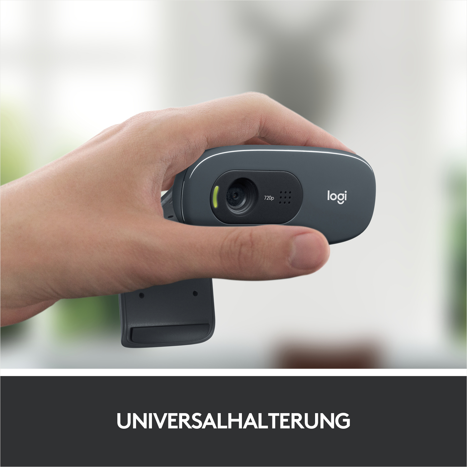 Eine Hand hält eine dunkelgraue Webcam mit Linse und Logitech-Logo.