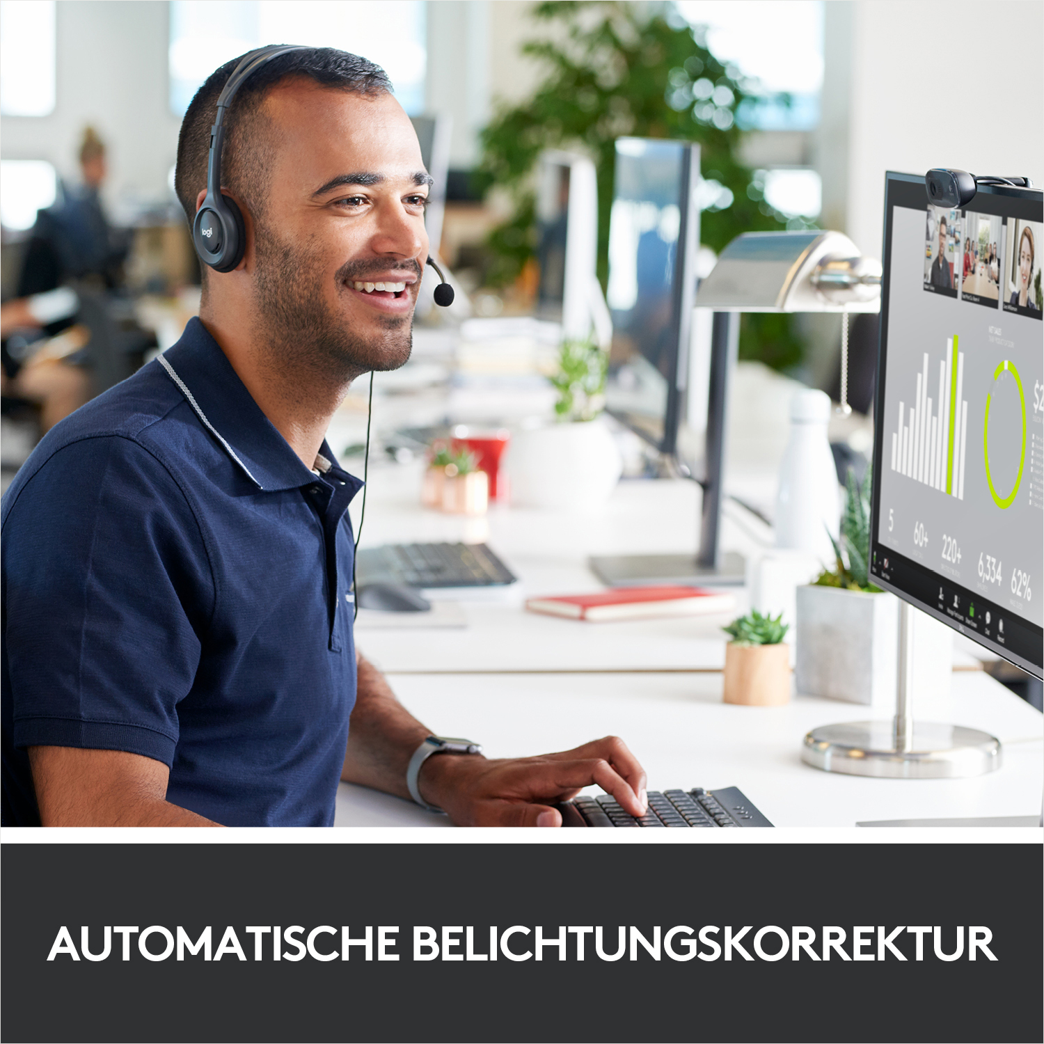 Ein Mann in blauem Hemd und Headset lächelt vor einem Computerbildschirm.