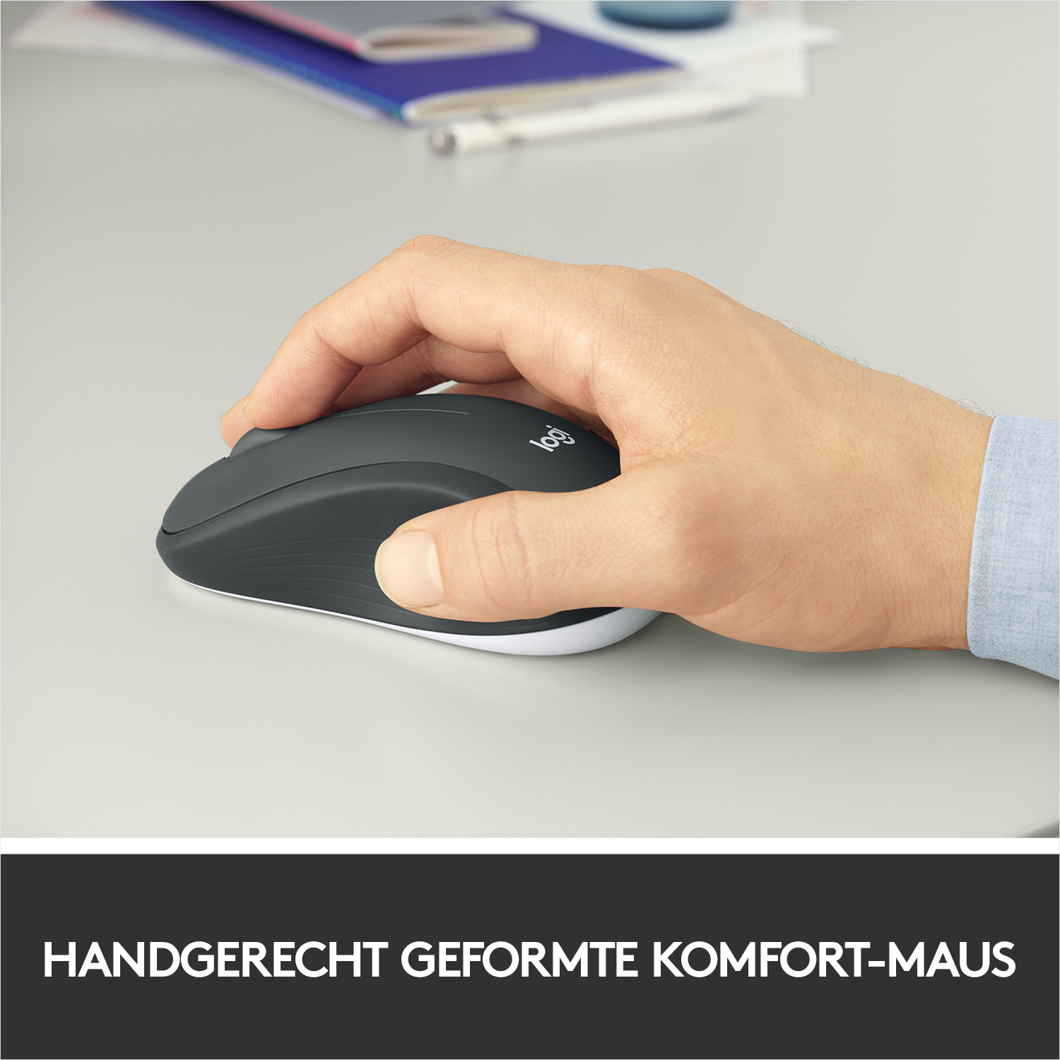 Eine Hand, die eine dunkelgraue Logitech-Maus auf einer hellgrauen Oberfläche hält.