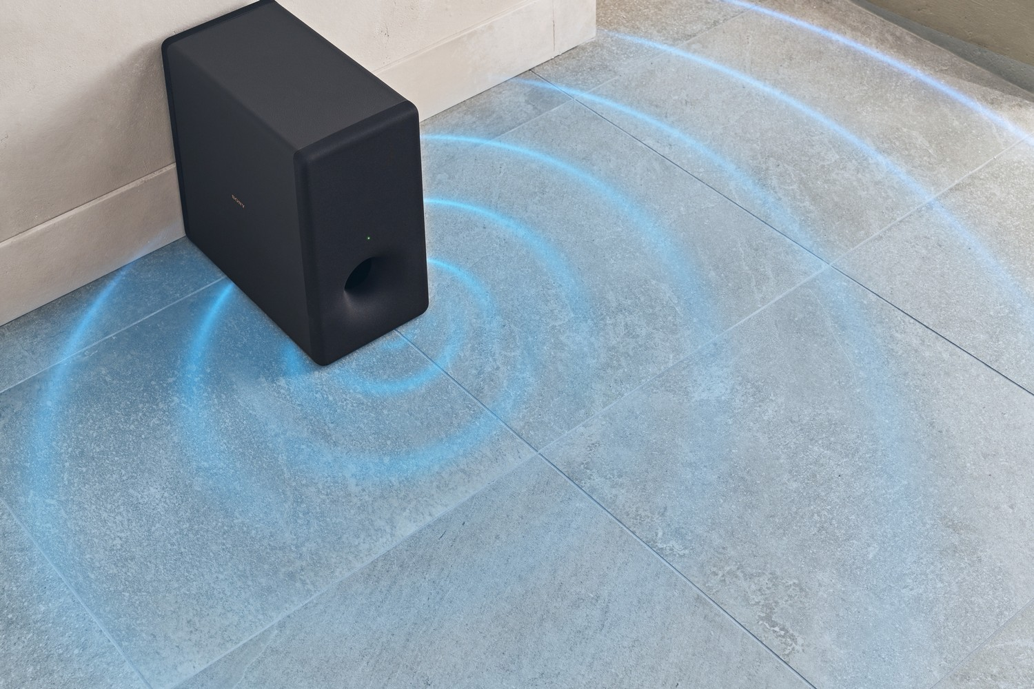 Subwoofer negro cerca de una pared, efecto de onda de sonido azul en baldosas grises.