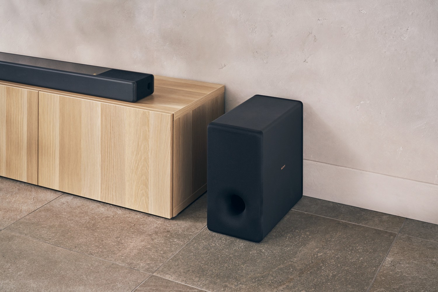 Salón moderno con barra de sonido y subwoofer. Armario de madera y paredes claras.