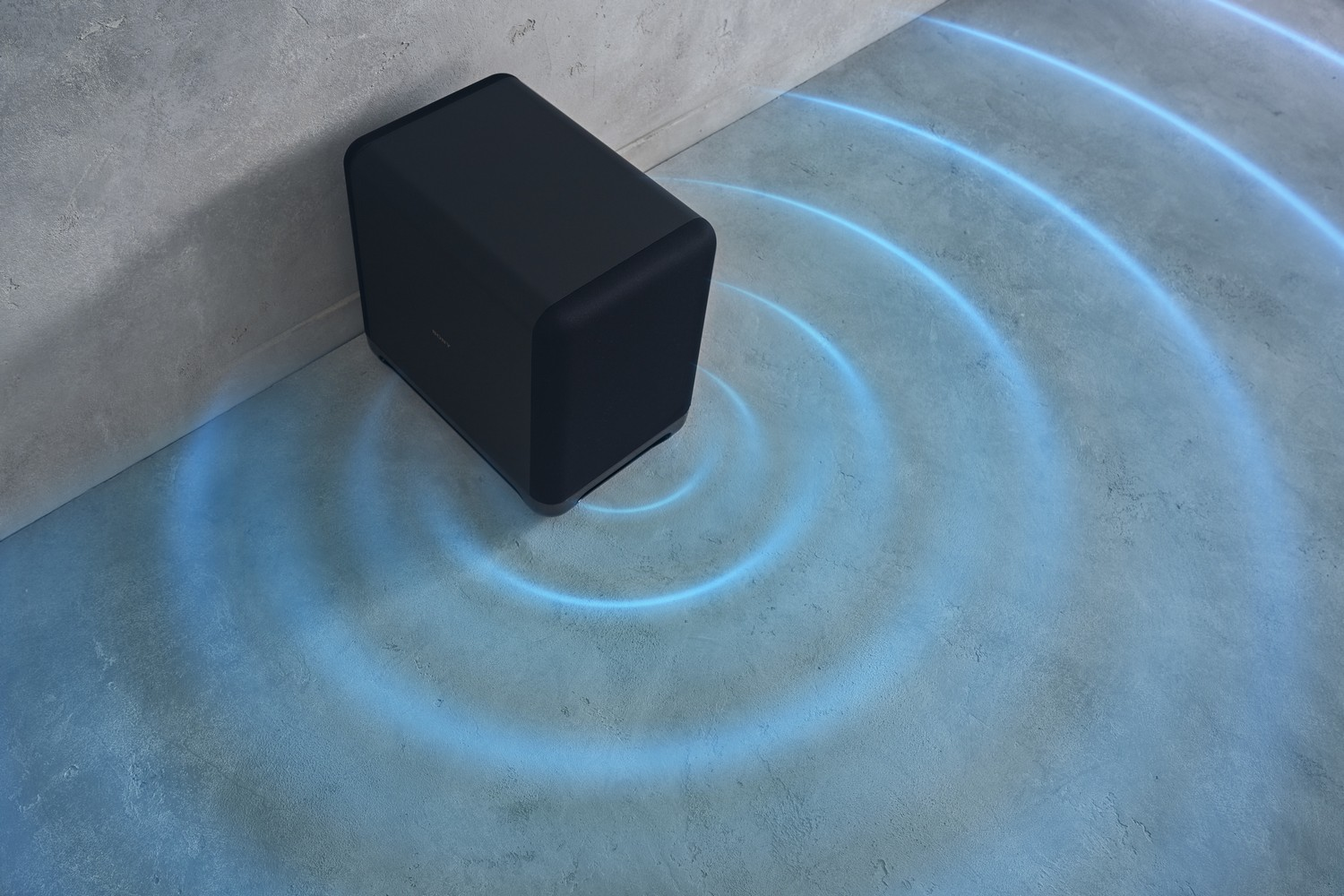 Altavoz subwoofer negro en un suelo de hormigón con líneas de onda azul.