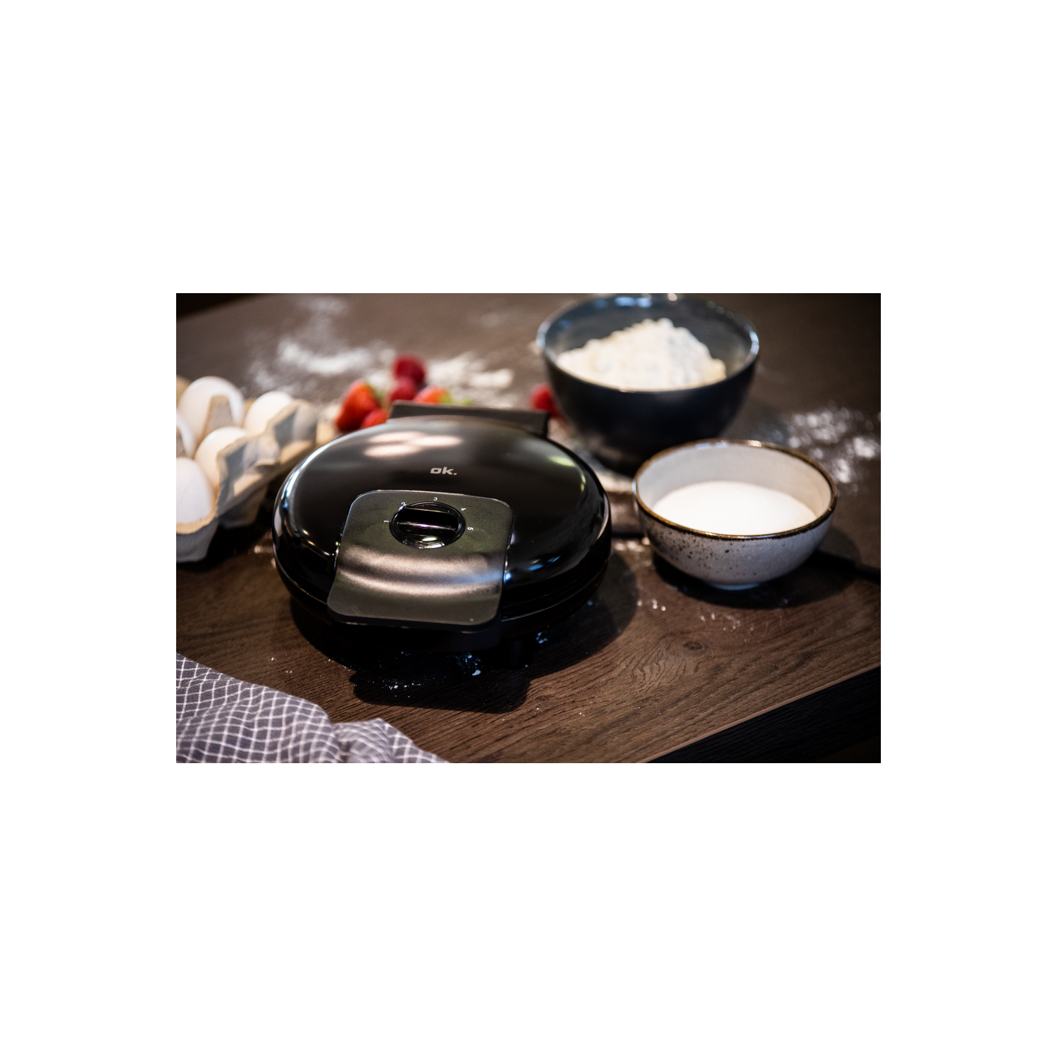 Una máquina para hacer gofres negra con ingredientes sobre mesa de madera.