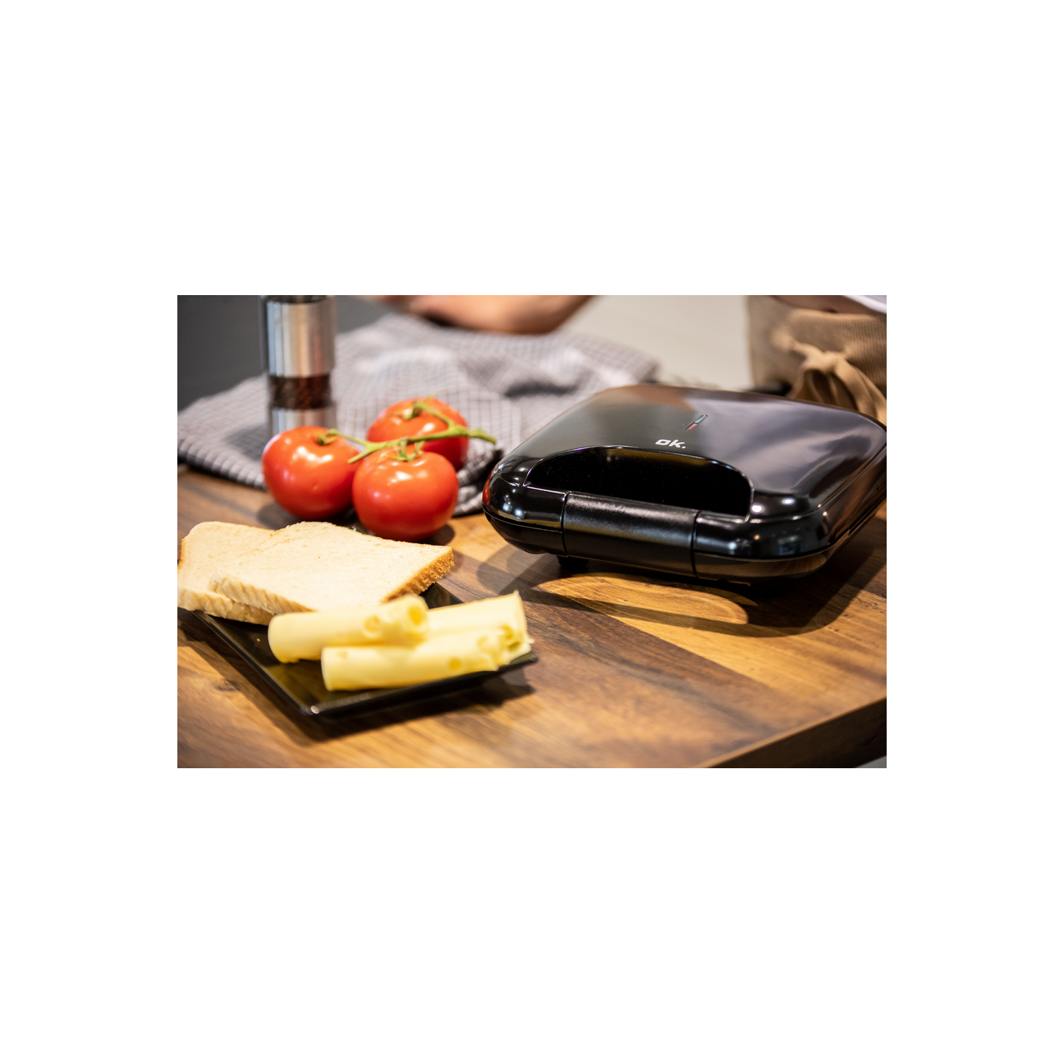 Sandwichera con pan, queso y tomates en una mesa de madera.