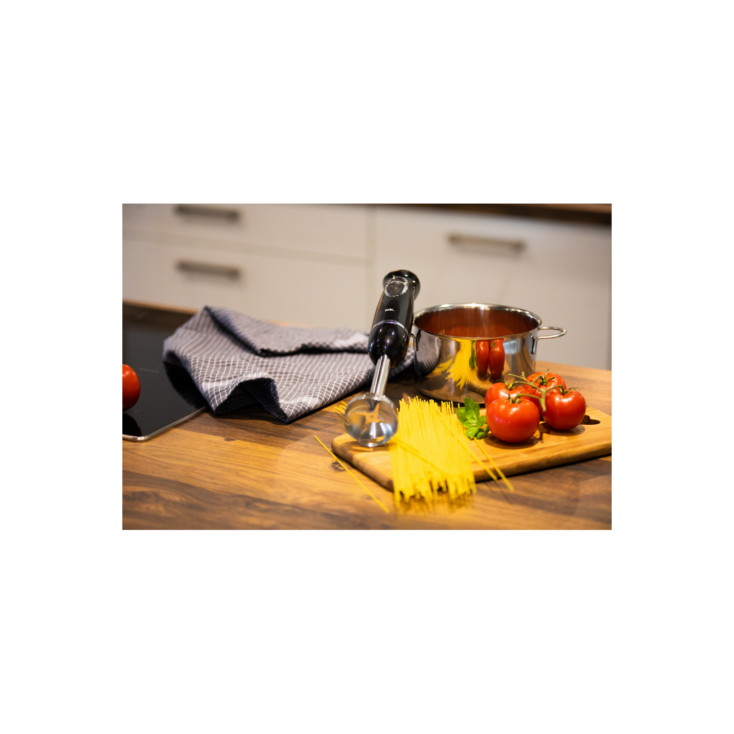 Licuadora, tomates, pasta y una olla sobre una superficie de madera en la cocina.