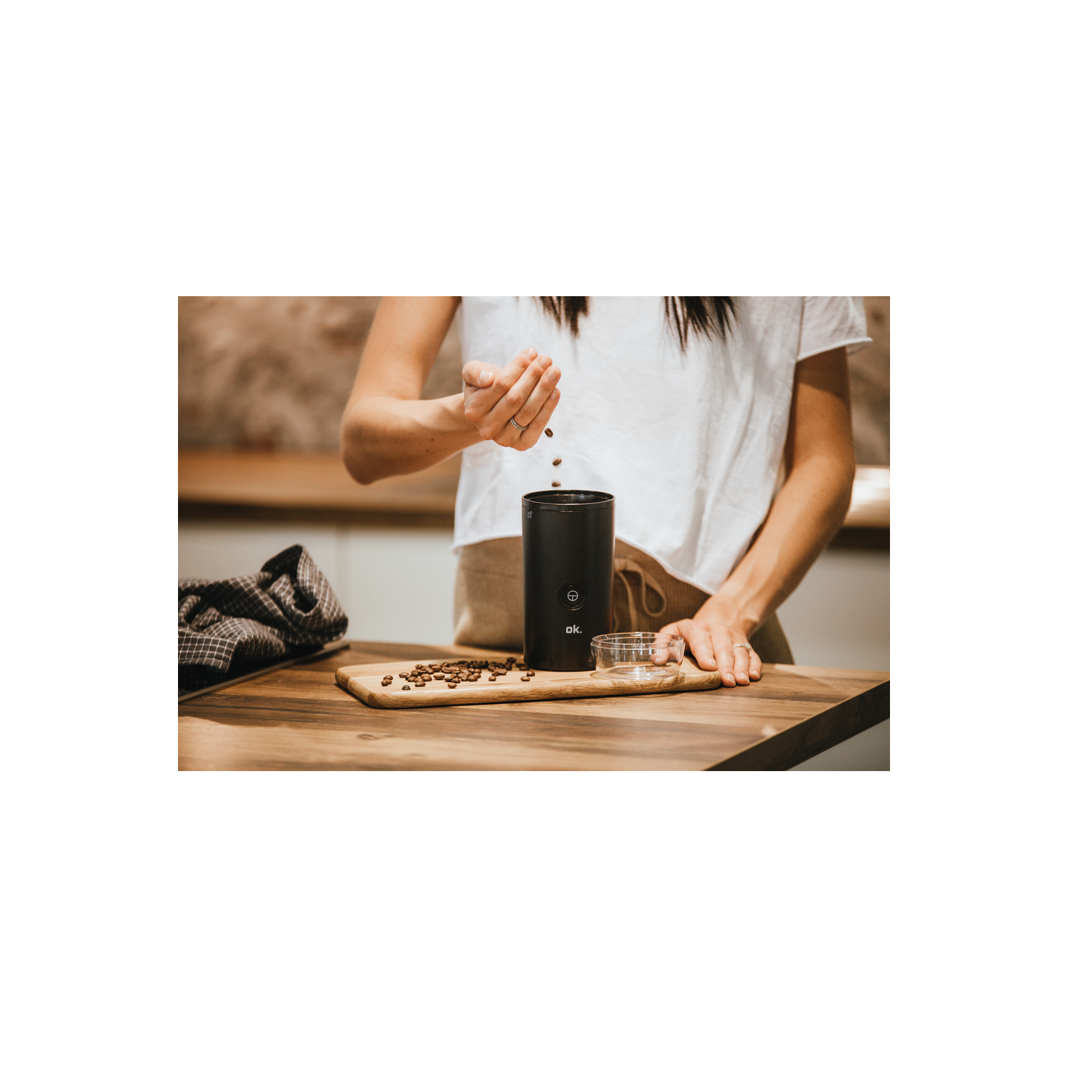 Manos de mujer vertiendo granos de café en un molinillo negro sobre una tabla de madera.