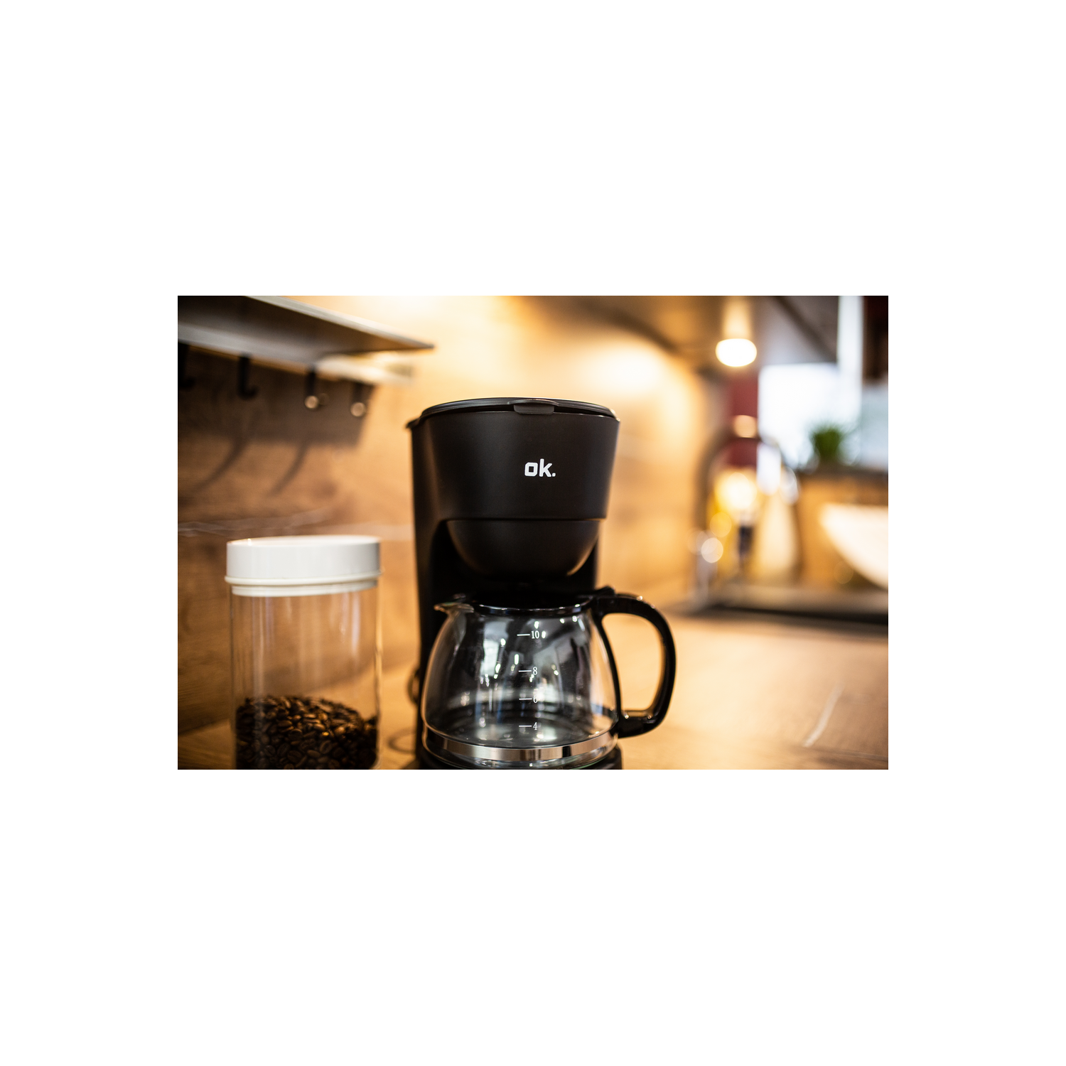 Una cafetera negra con una jarra de vidrio, junto a un frasco de granos de café.