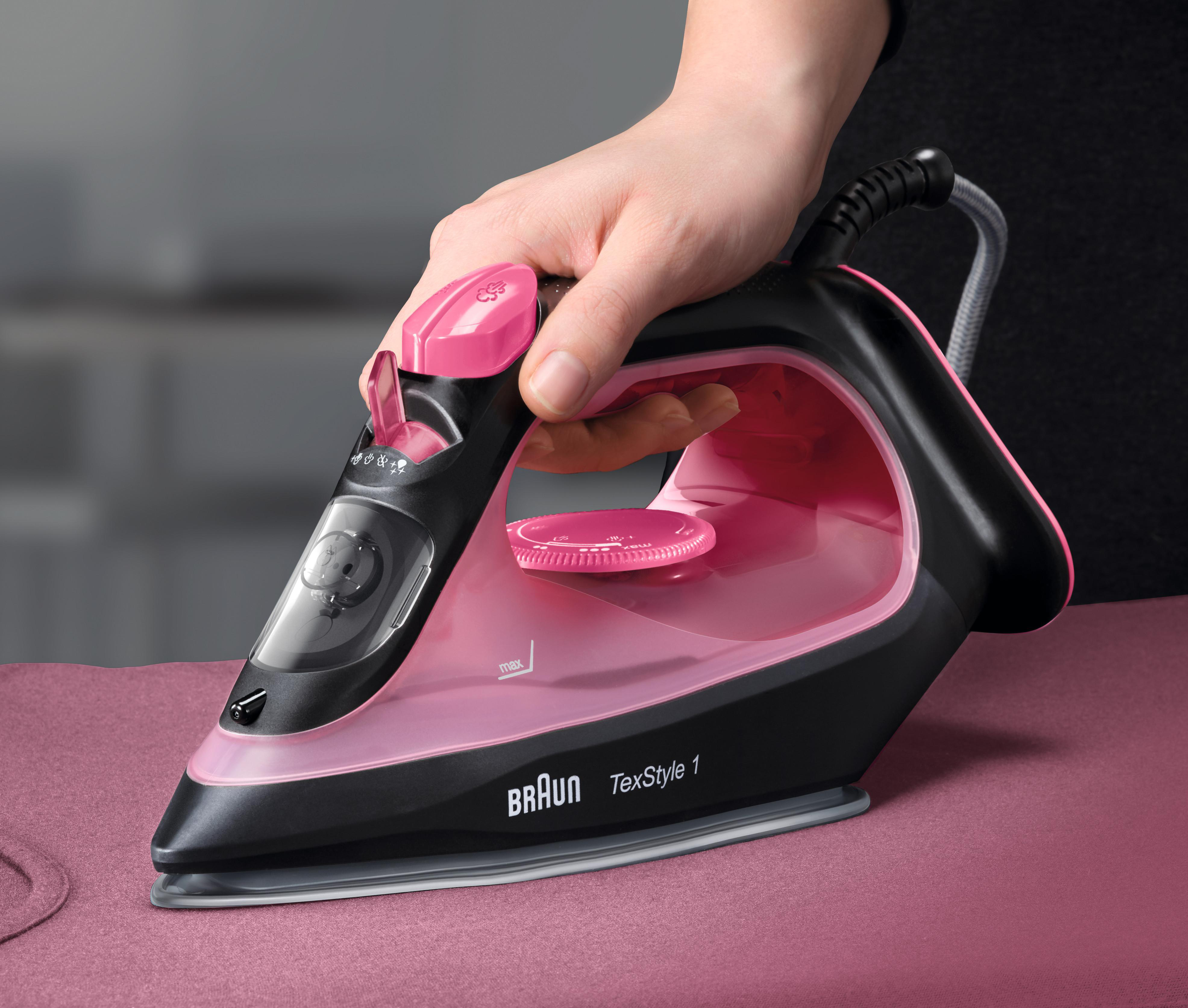 Eine Hand hält ein rosa-schwarzes Bügeleisen von Braun auf einem rosa Bügelbrett.