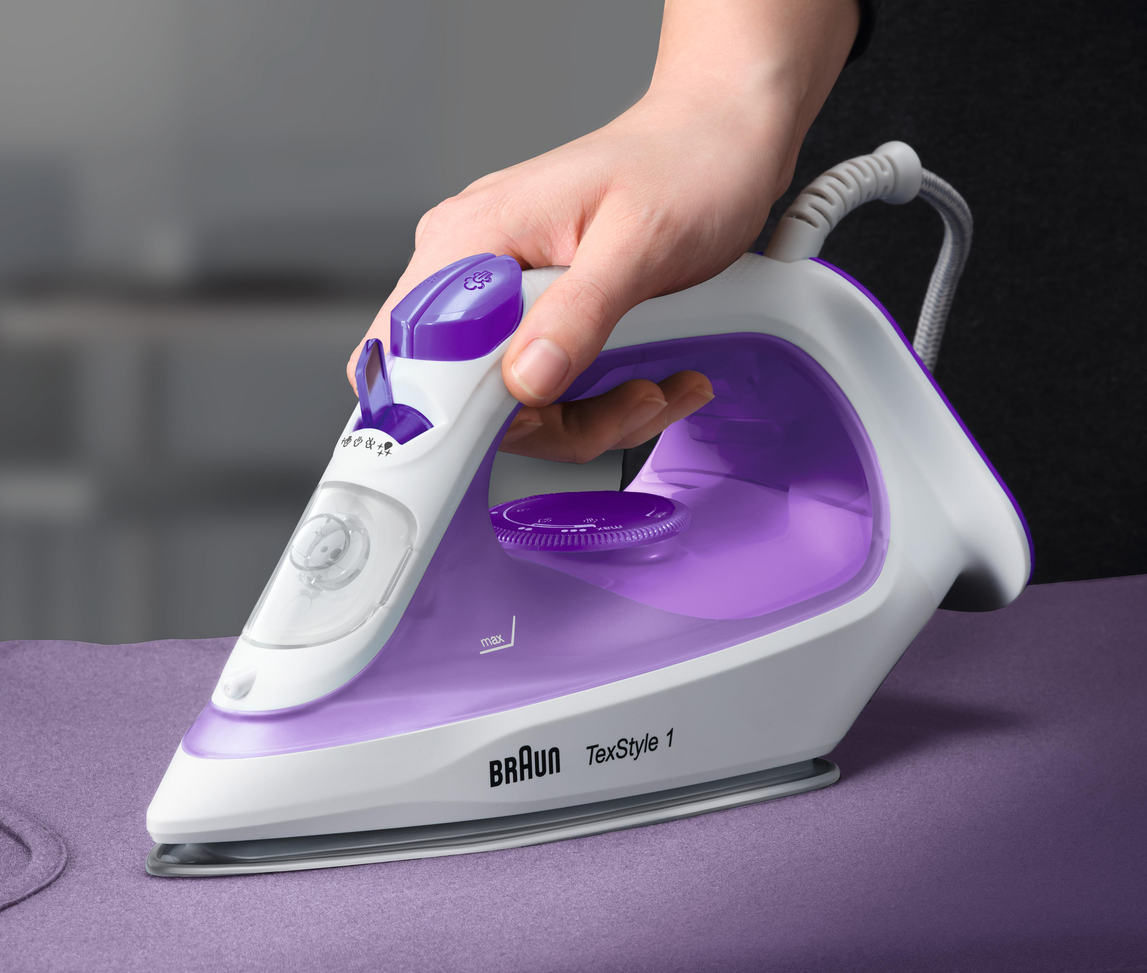 Weißes und lila Bügeleisen auf einem lila Bügelbrett. Hand hält das Bügeleisen. Braun TexStyle 1.