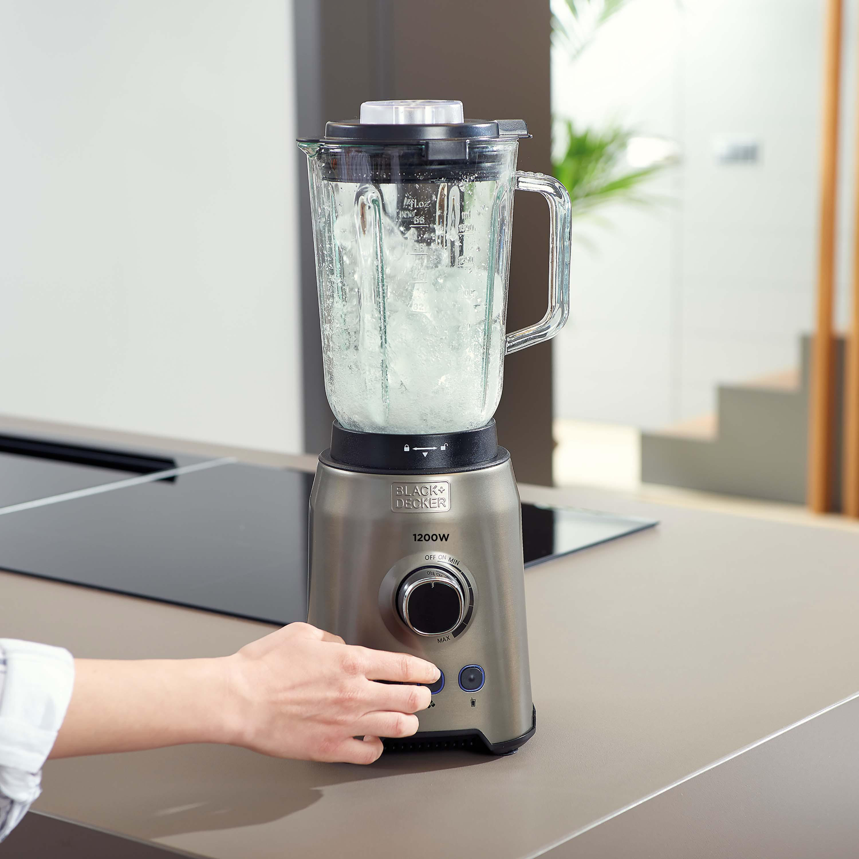 Silberner und schwarzer Mixer mit Eis und einer Hand, die einen Knopf drückt, auf einer Küchenarbeitsplatte.