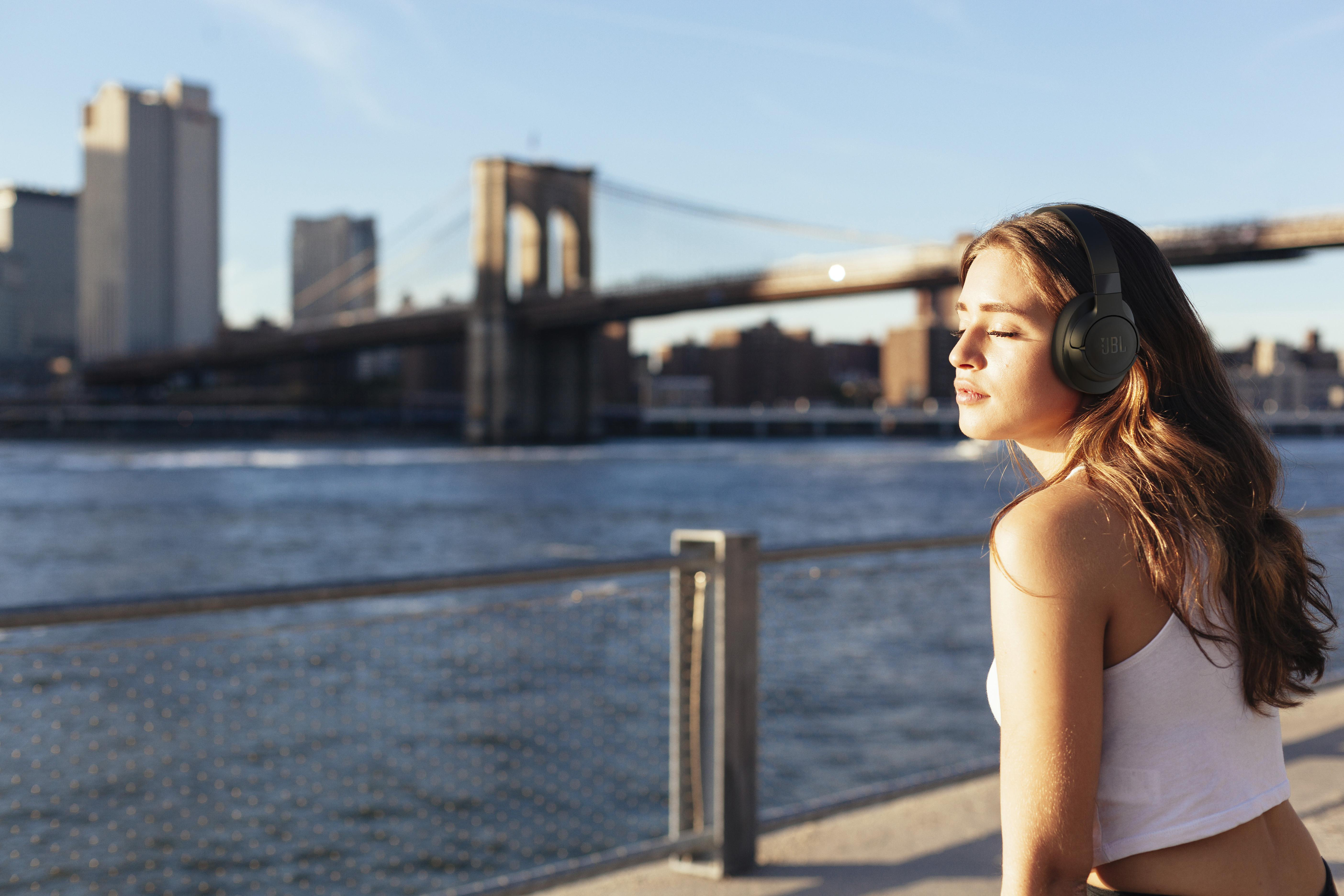 Frau mit Kopfhörern am Wasser, Brooklyn Bridge im Hintergrund.
