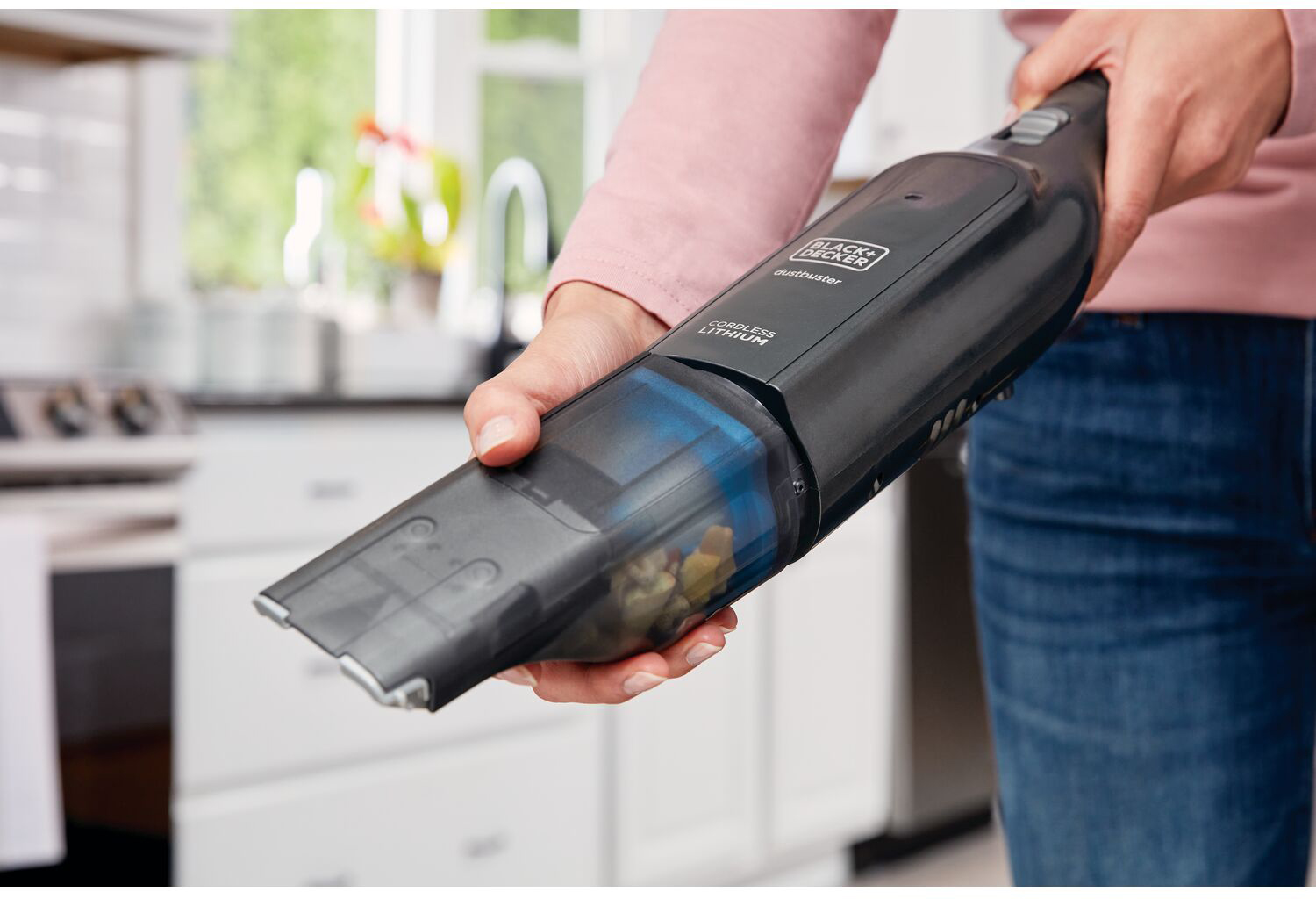 Person holding a black handheld vacuum cleaner, cleaning. A kitchen setting with a white oven is visible.