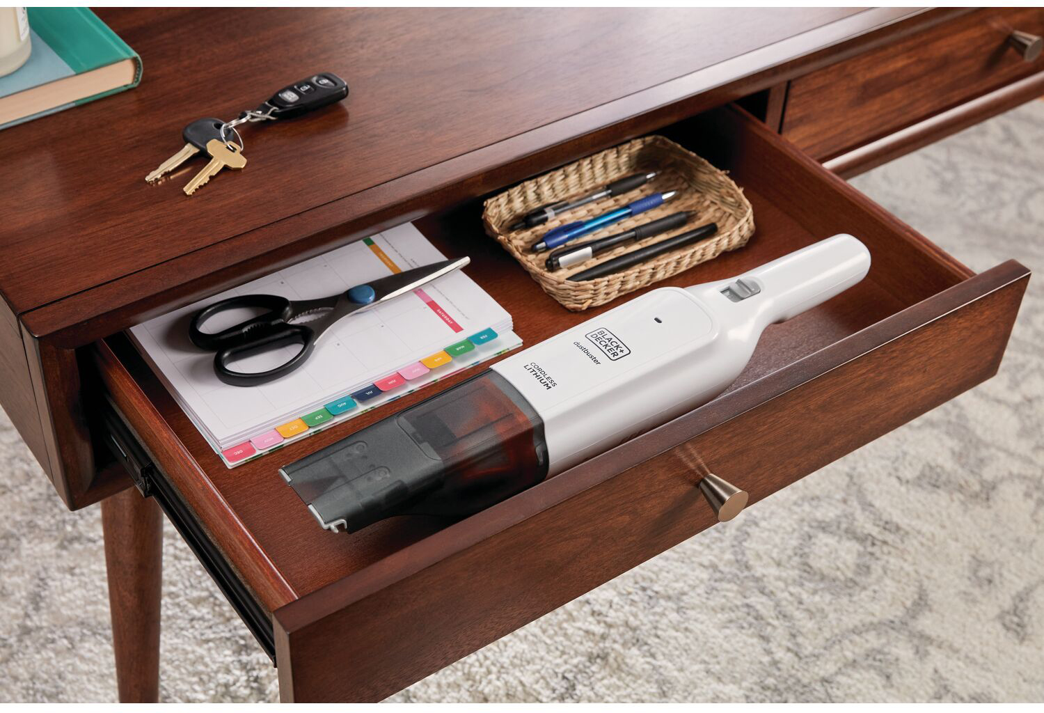 Open drawer with office supplies: scissors, pens, vacuum and keys.