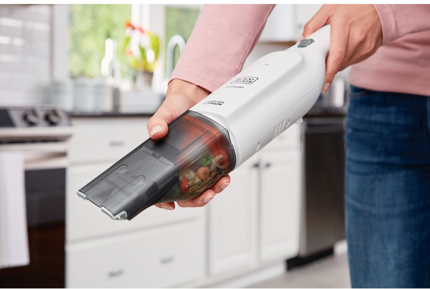 A person holding a handheld vacuum cleaner, white and black, cleaning a kitchen counter. 