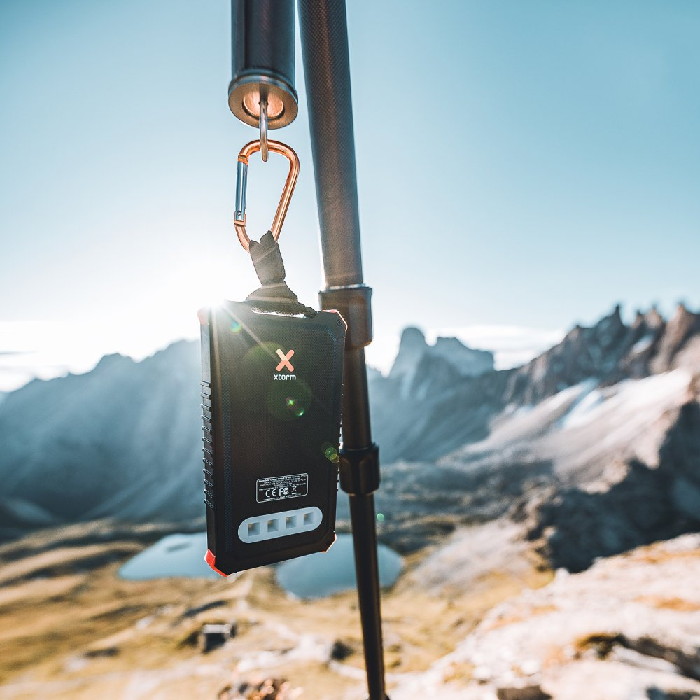Ein schwarzer Lautsprecher, der an einem Karabiner an einem Stativ hängt, Berge im Hintergrund.
