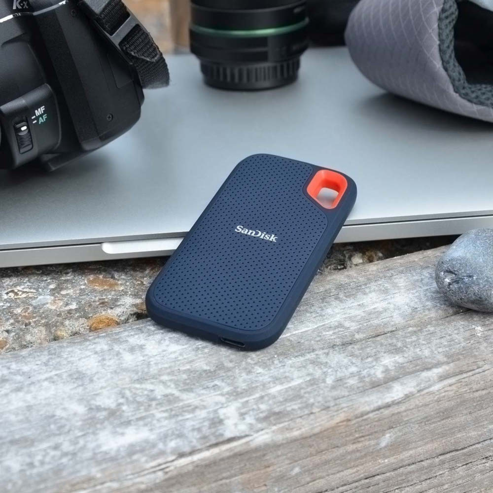 Un disque dur portable bleu et gris foncé posé sur du bois et un ordinateur portable.