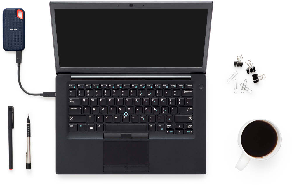 Ordinateur portable, disque dur externe, stylos et une tasse de café sur une surface blanche, vue de dessus.