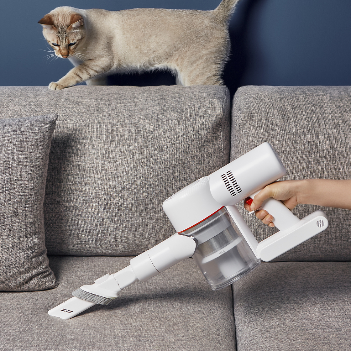 Weißer und roter Staubsauger auf Sofa, Katze in der Nähe.