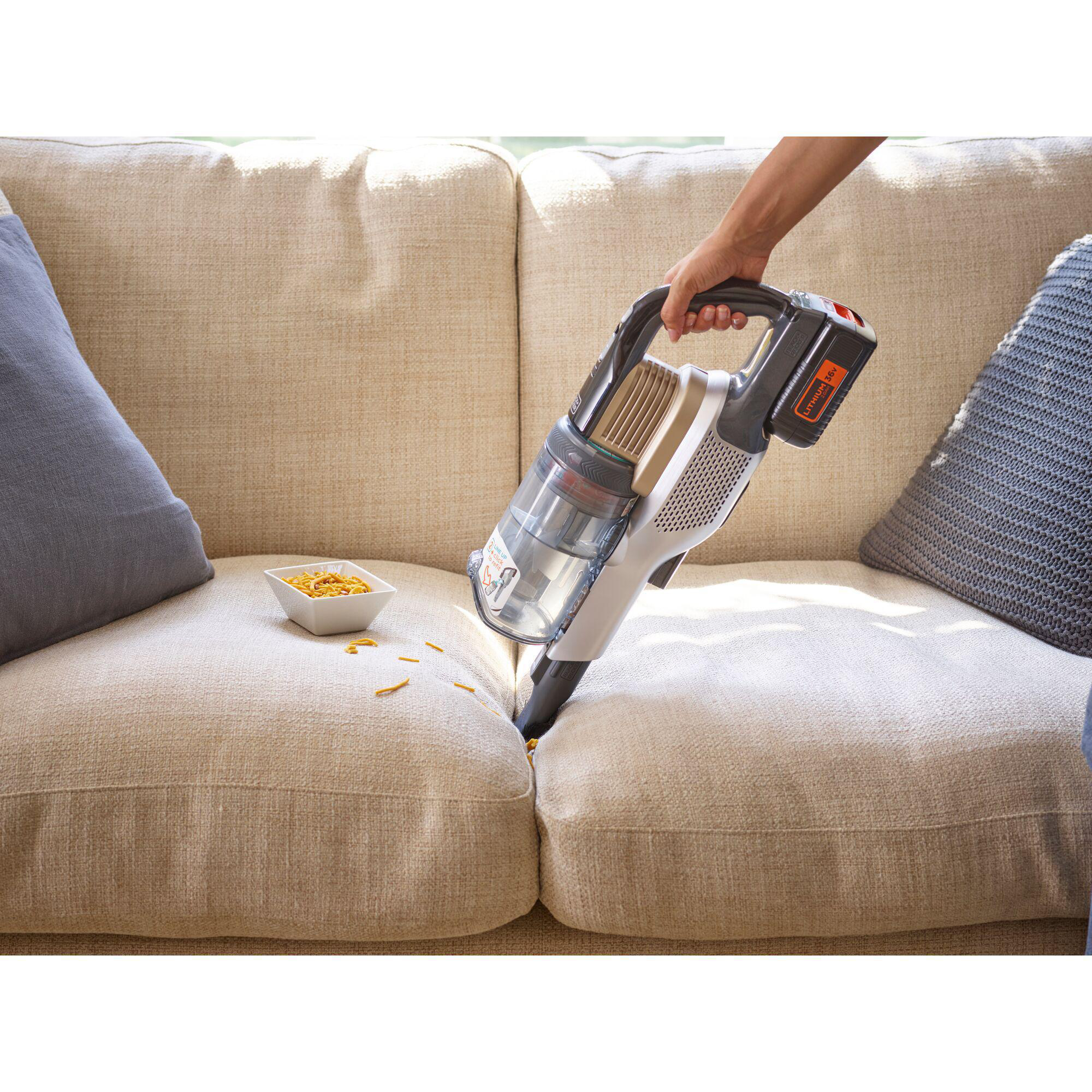 Hand saugt Sofa ab. Schüssel Pasta. Graue und beige Kissen.