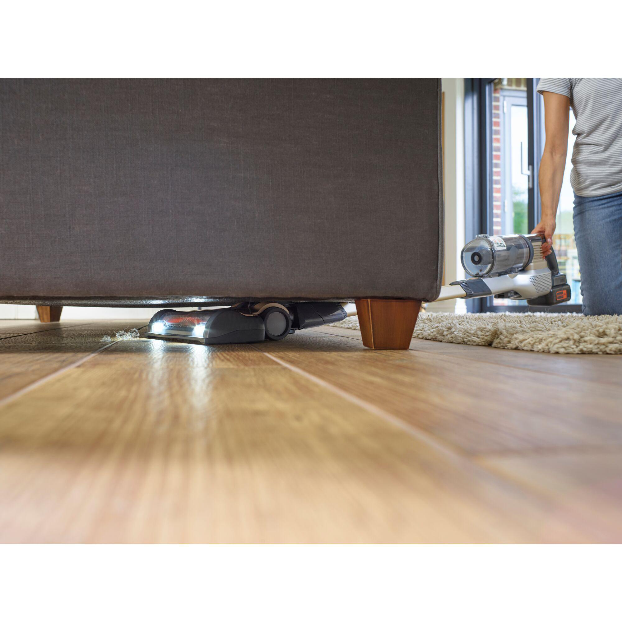 Ein Staubsauger reinigt unter einem Sofa, auf einem Holzboden.