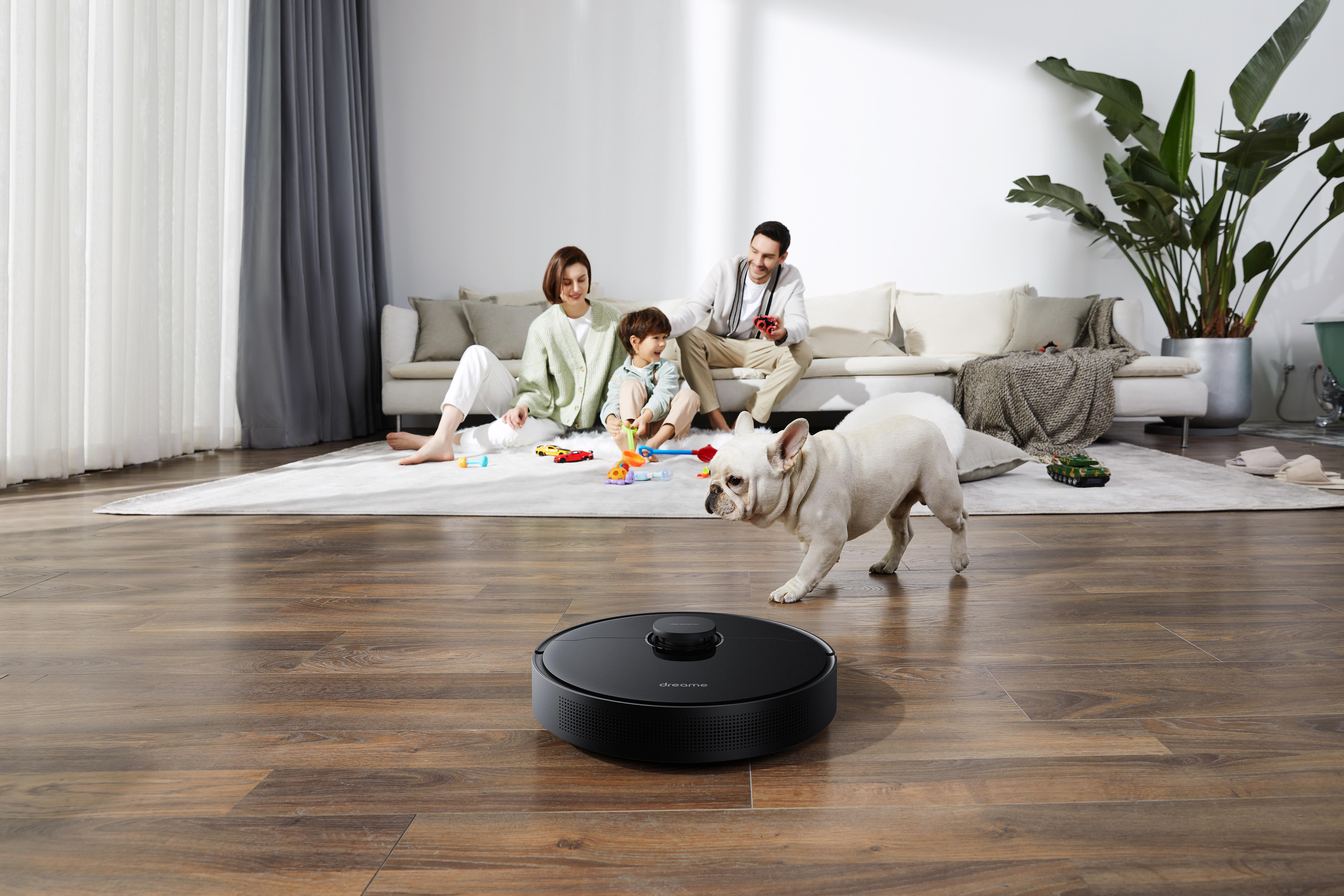 Eine Familie mit Hund und Roboter-Staubsauger auf Holzboden im Wohnzimmer.