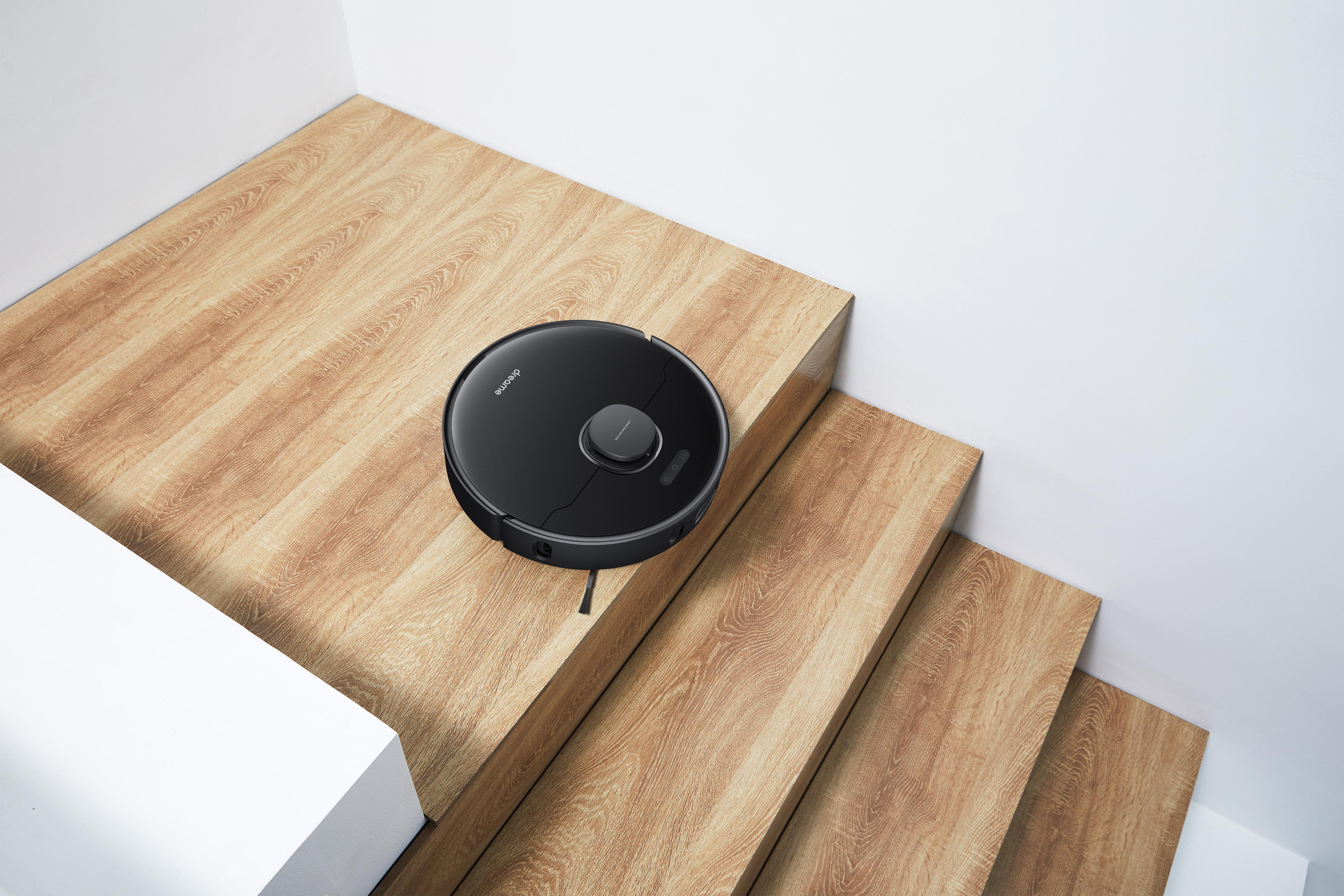 Ein schwarzer Dreame-Roboter-Staubsauger auf Holztreppen, weiße Wände.