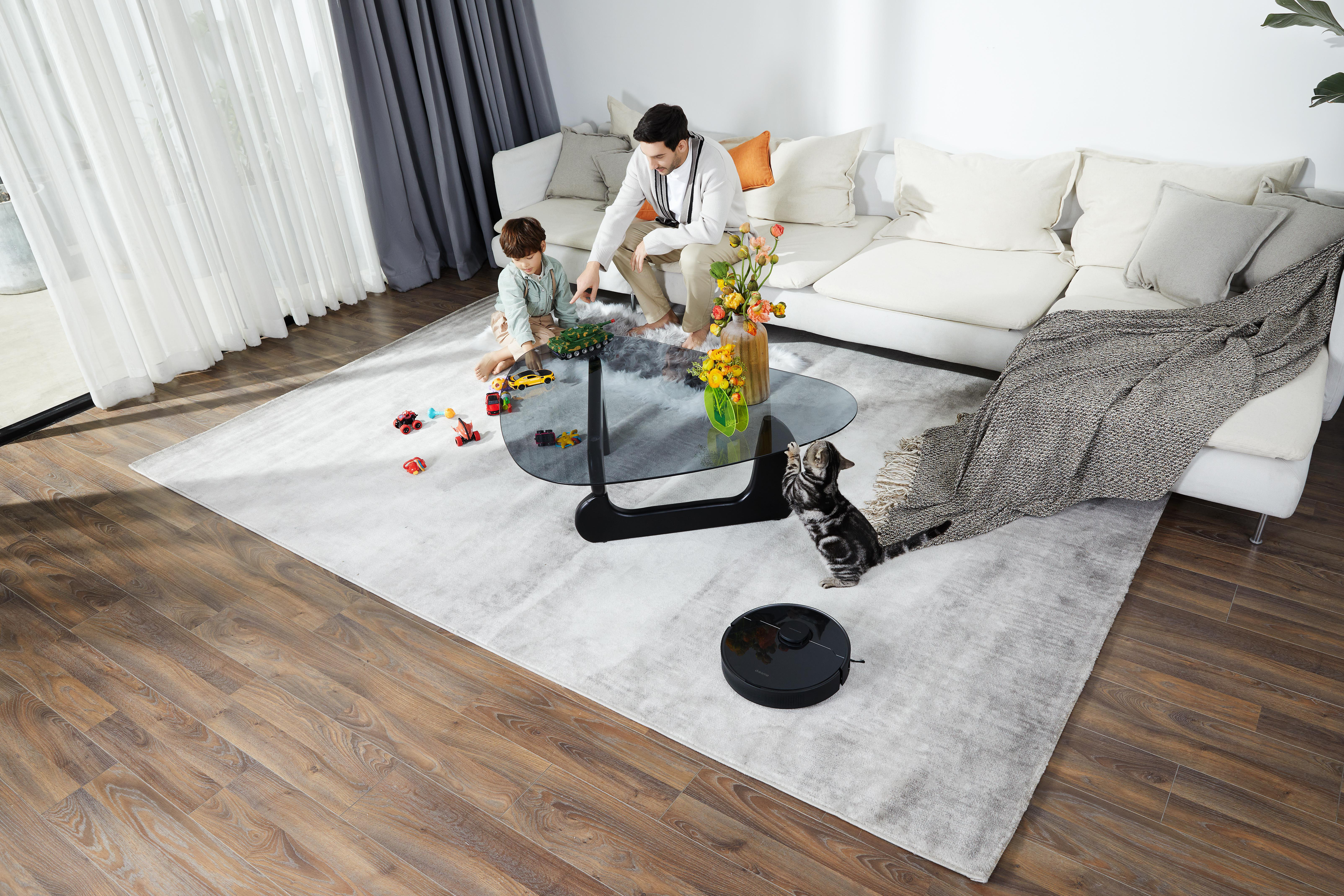 Familie im Wohnzimmer mit Roboterstaubsauger und Spielzeug auf dem Boden.