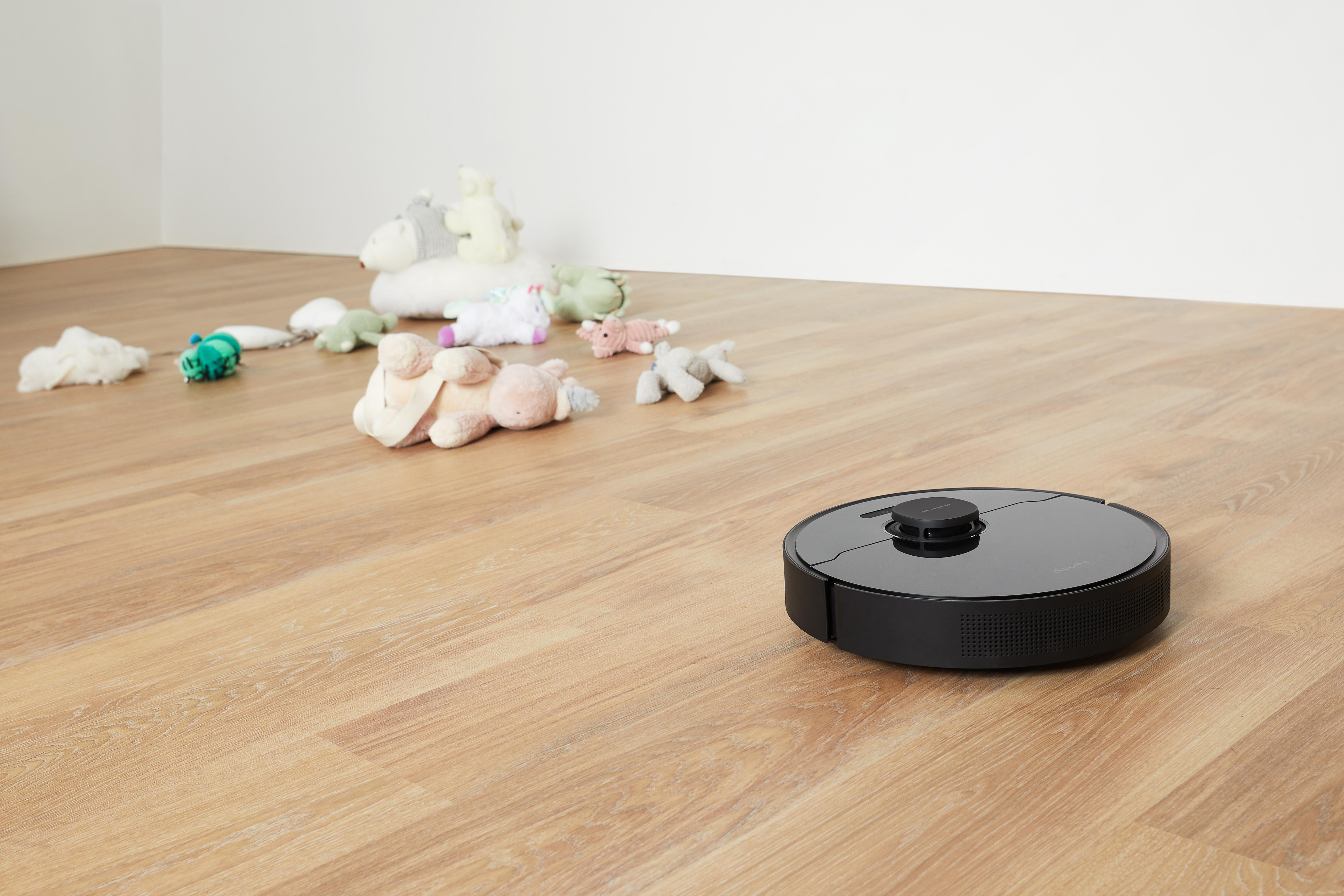 Ein schwarzer Roboter-Staubsauger auf einem Holzboden, mit Spielzeug im Hintergrund.
