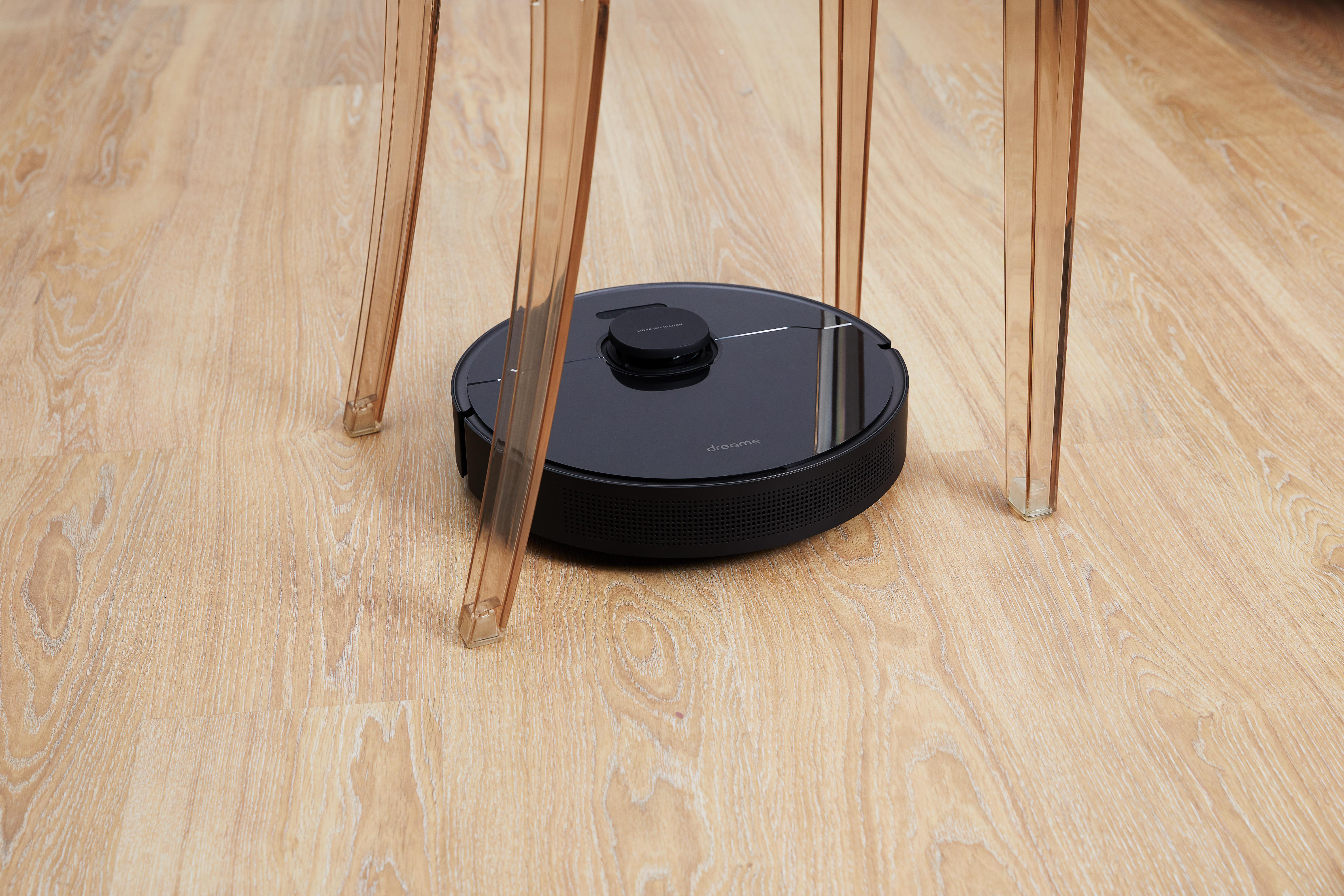 Ein schwarzer Roboter-Staubsauger steht unter einem Tisch mit transparenten Acrylbeinen.