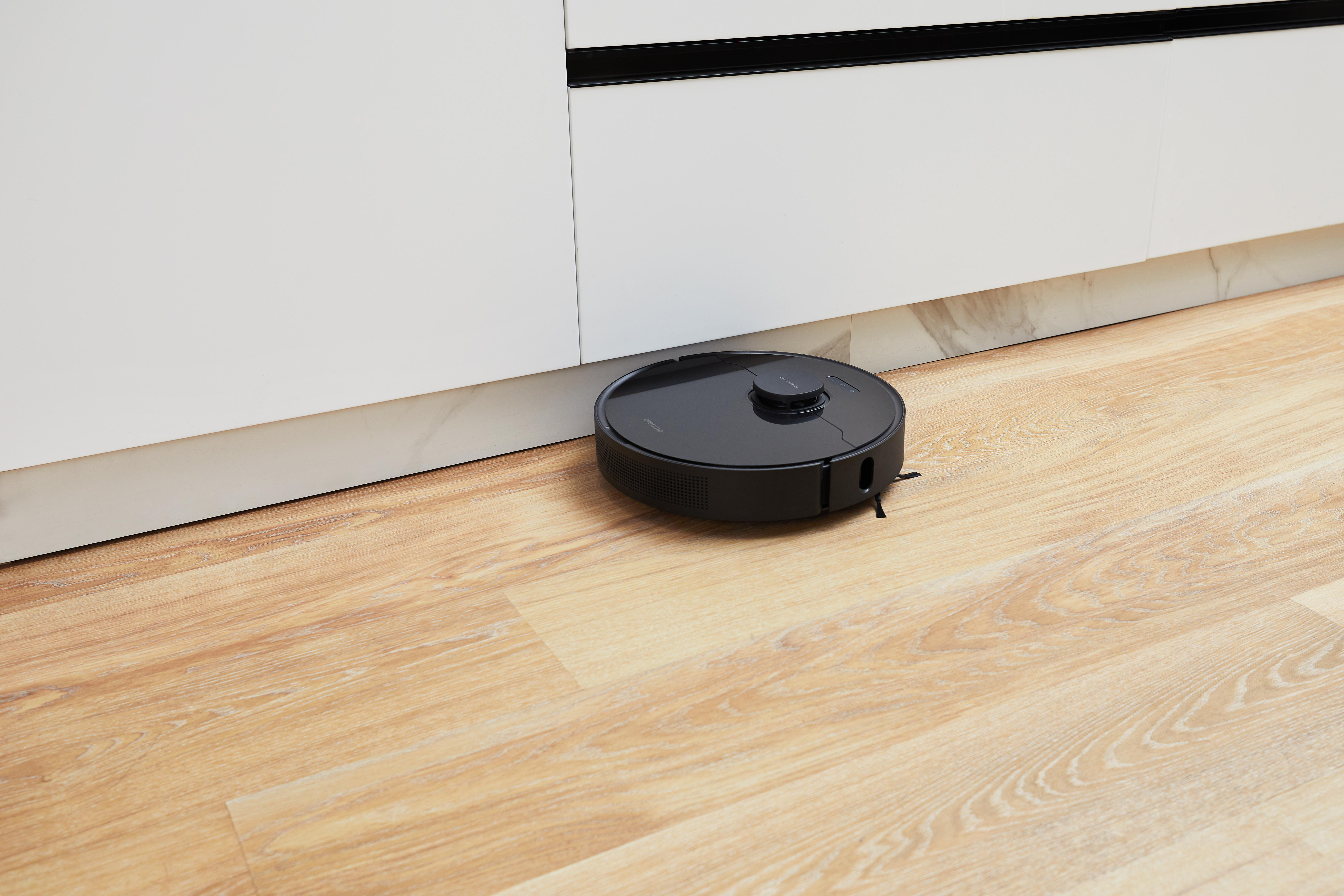 Schwarzer Roboter-Staubsauger auf Holzboden, in der Nähe eines weißen Schranks.