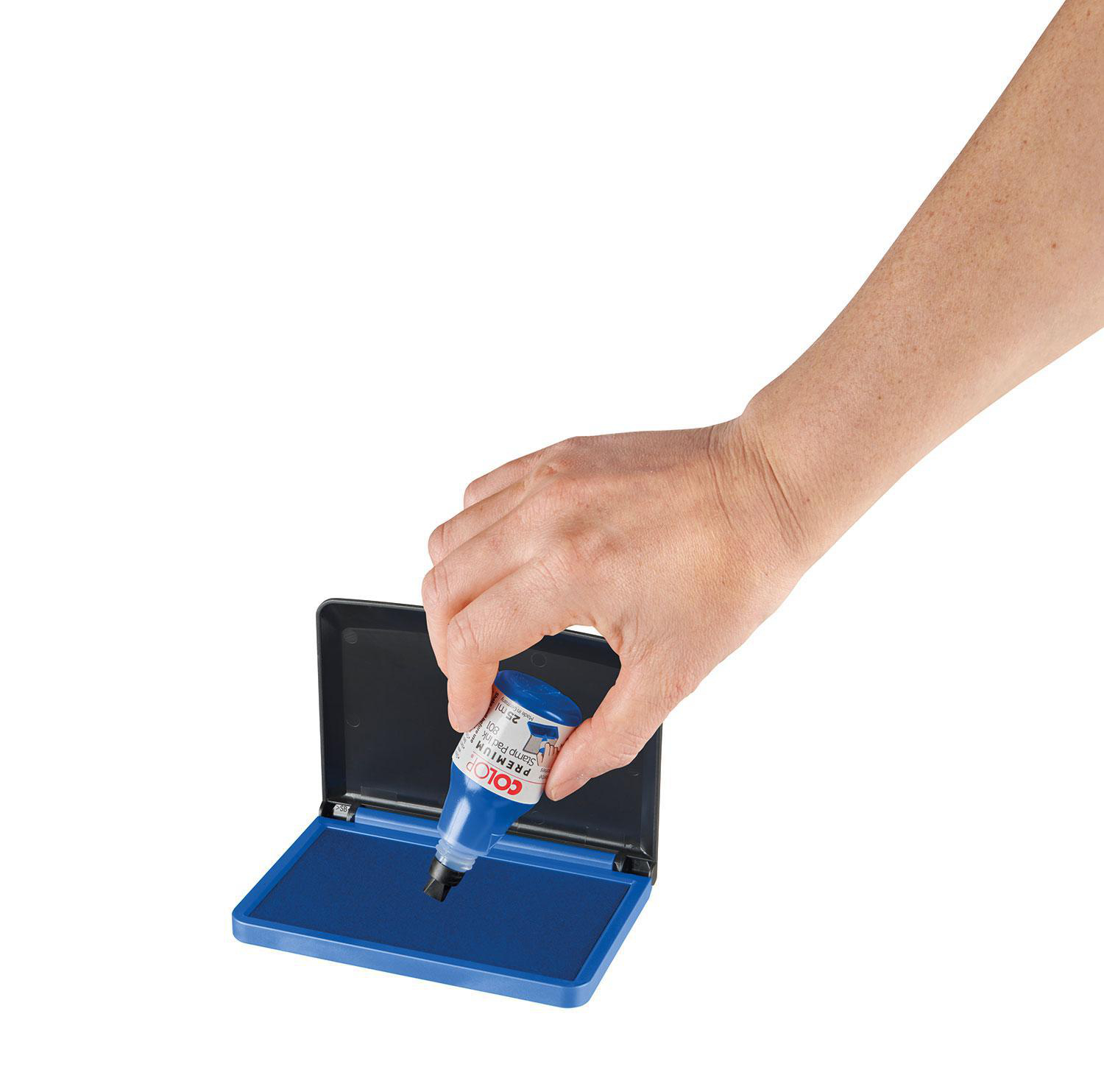 Eine Hand hält eine blaue Tintenflasche über einem blauen Stempelkissen. Ein schwarzes Stempelkissen ist geöffnet.
