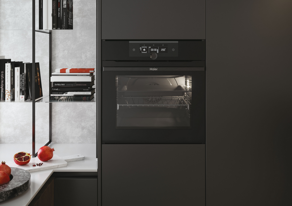 Horno negro moderno con pantalla y puerta abierta. Granadas y libros en la encimera.