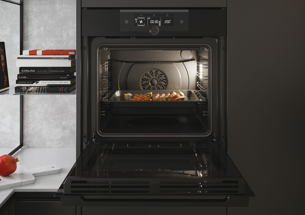 Horno abierto con comida dentro, iluminado. Encimera de cocina delante.