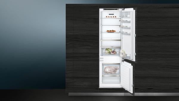 Offener Kühlschrank mit Lebensmitteln in Fächern, blau-grauer Hintergrund.