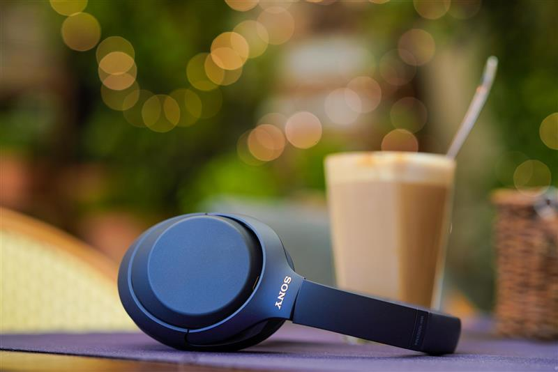 Black headphones on a table with a coffee and a blurred background.