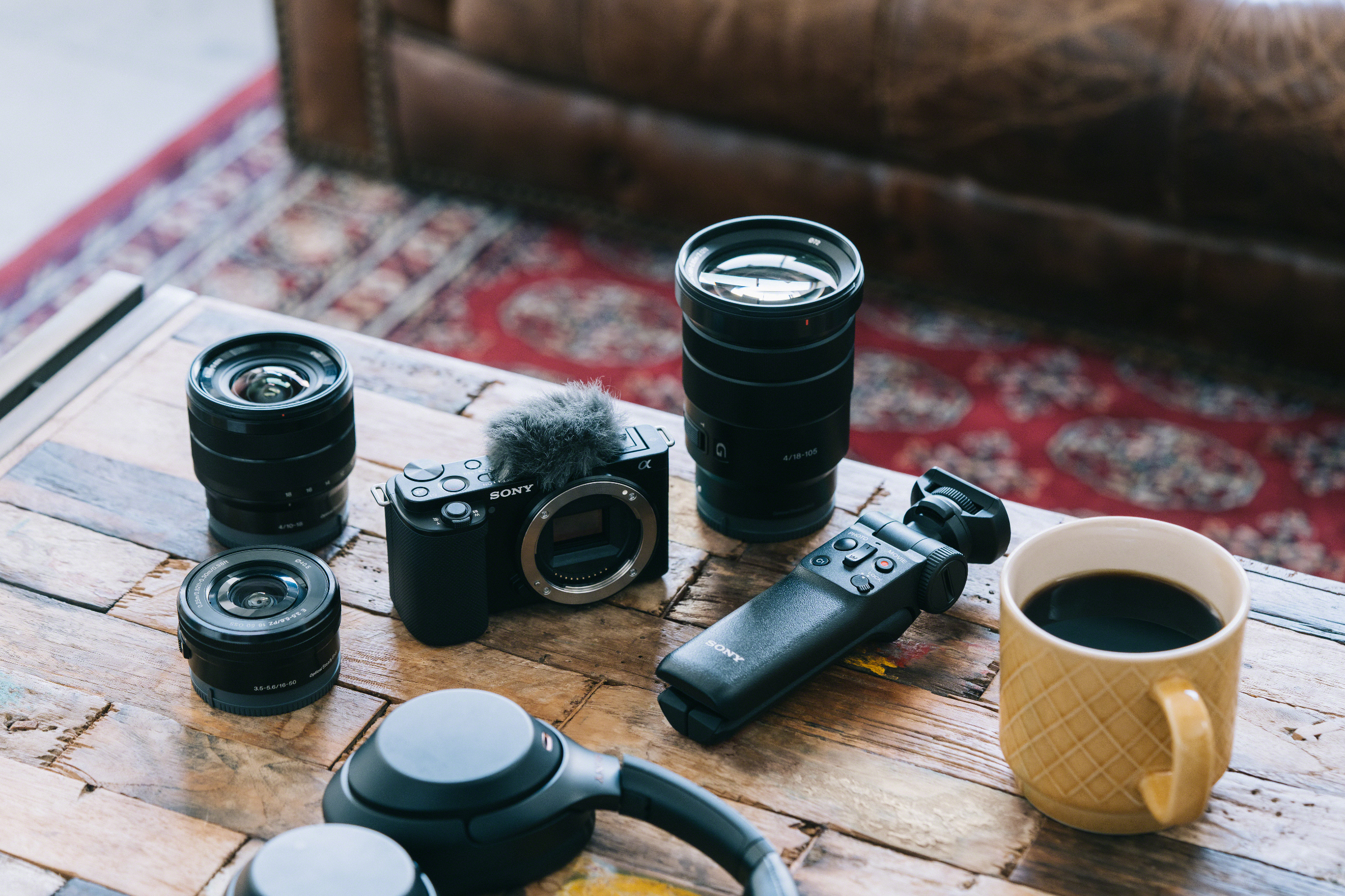 Un tavolo con obiettivi, una fotocamera, un microfono, un treppiede e una tazza di caffè.