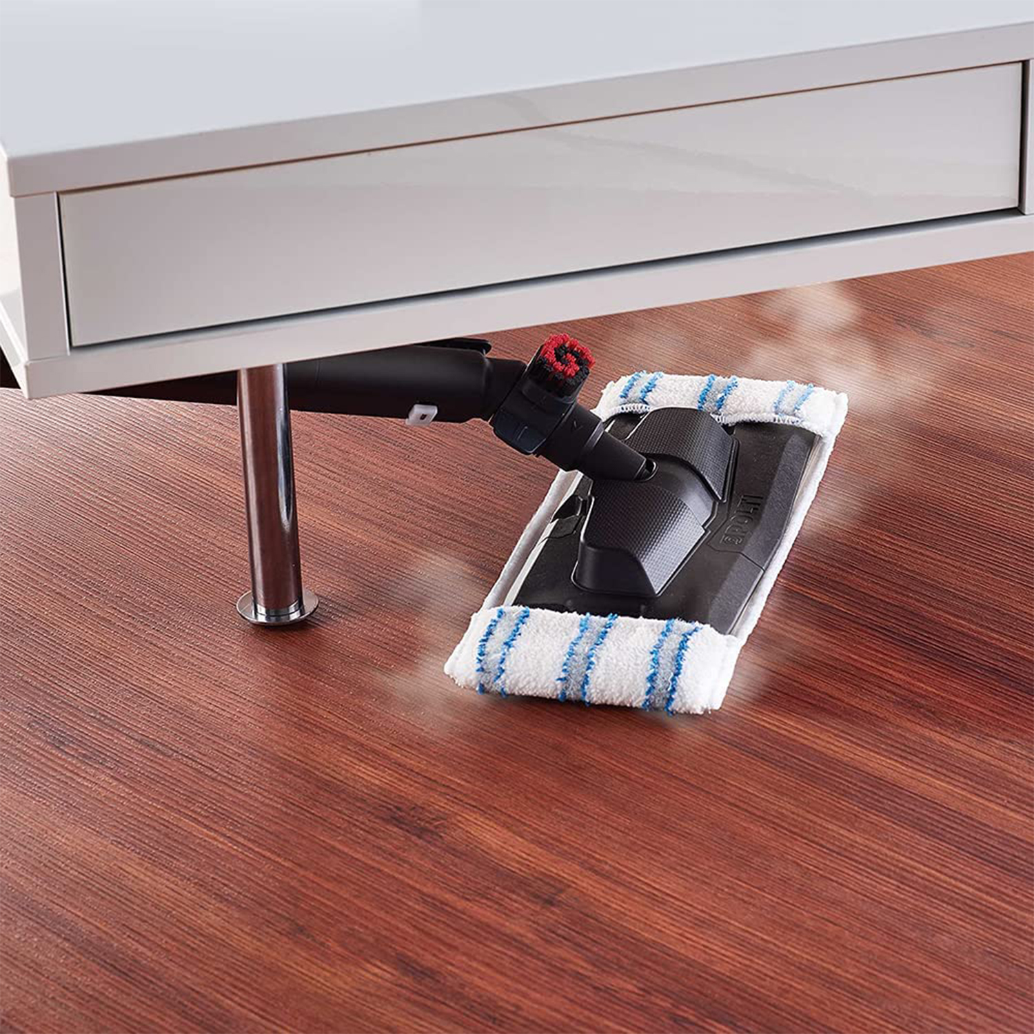 L'immagine mostra una scopa a vapore che pulisce un pavimento in legno, con un mobile bianco sopra.