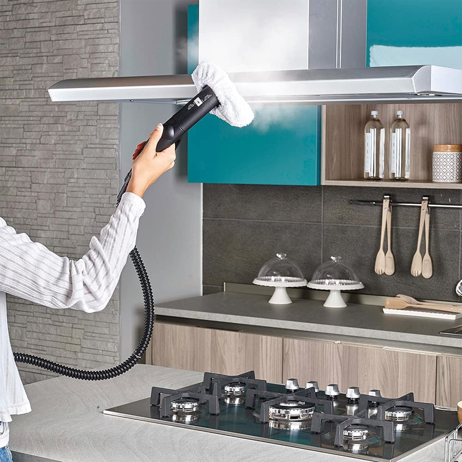 Persona che pulisce una cappa da cucina con un pulitore a vapore, vapore visibile.