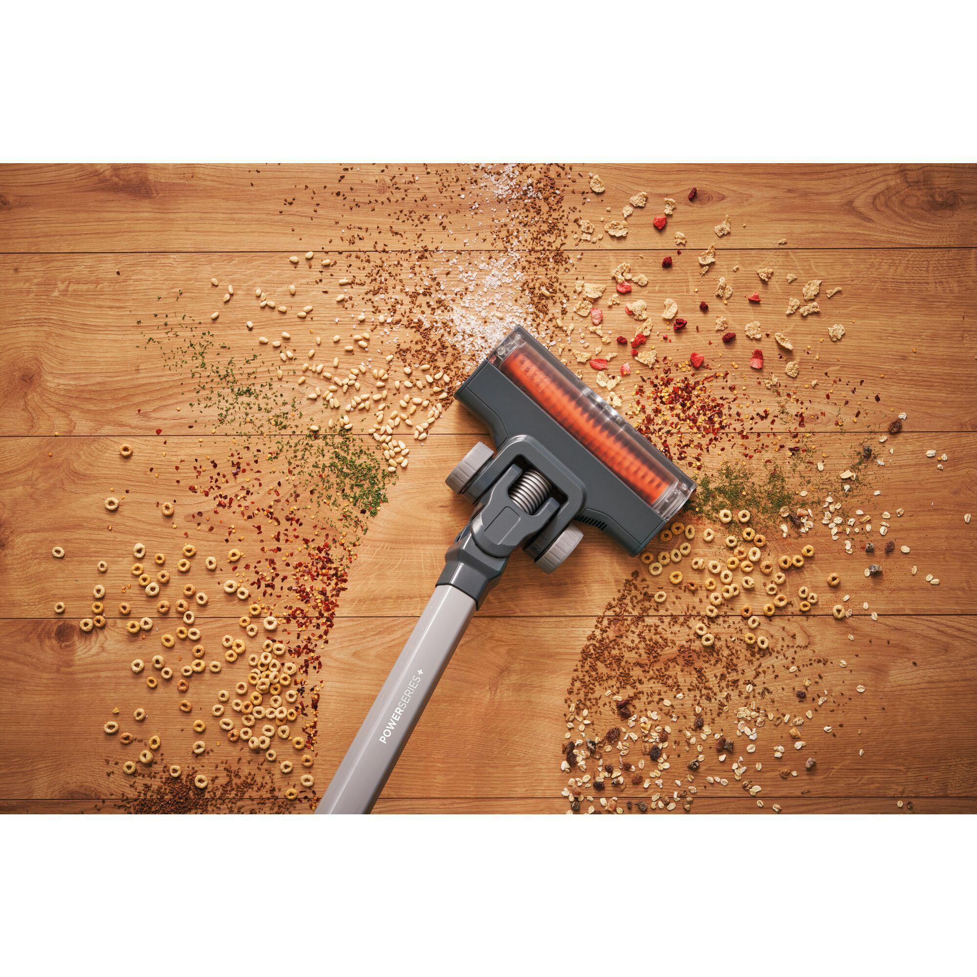 Staubsaugerkopf reinigt Holzboden, der mit Essensresten bedeckt ist.