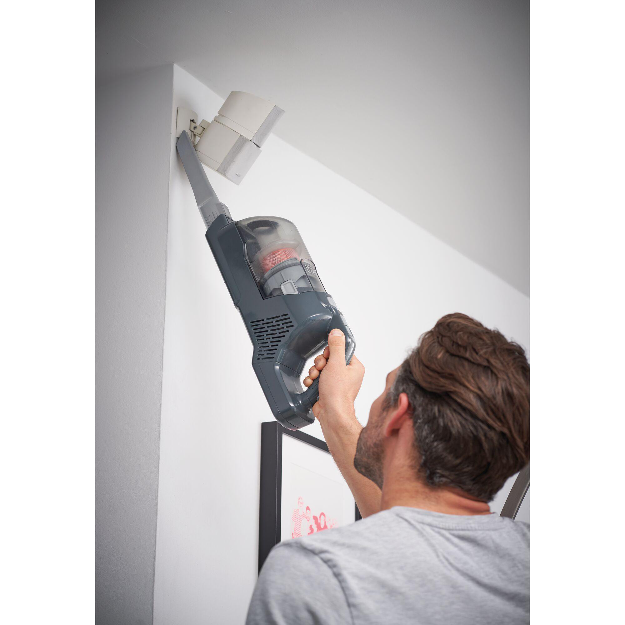 Ein Mann, der mit einem Handstaubsauger eine Wand absaugt. Die Wand ist weiß.