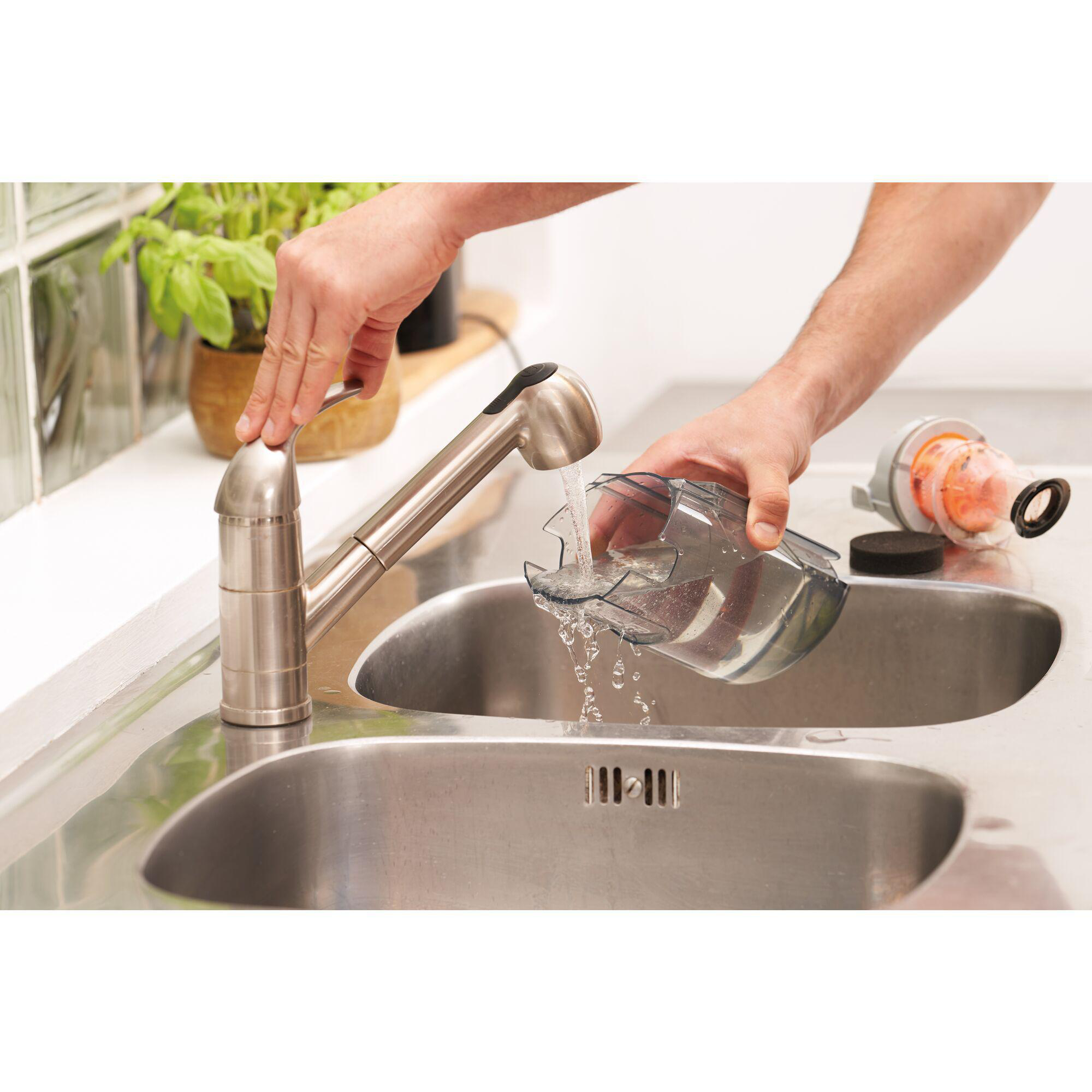 Hände spülen Staubsaugerteil unter silbernem Wasserhahn in einem Waschbecken.