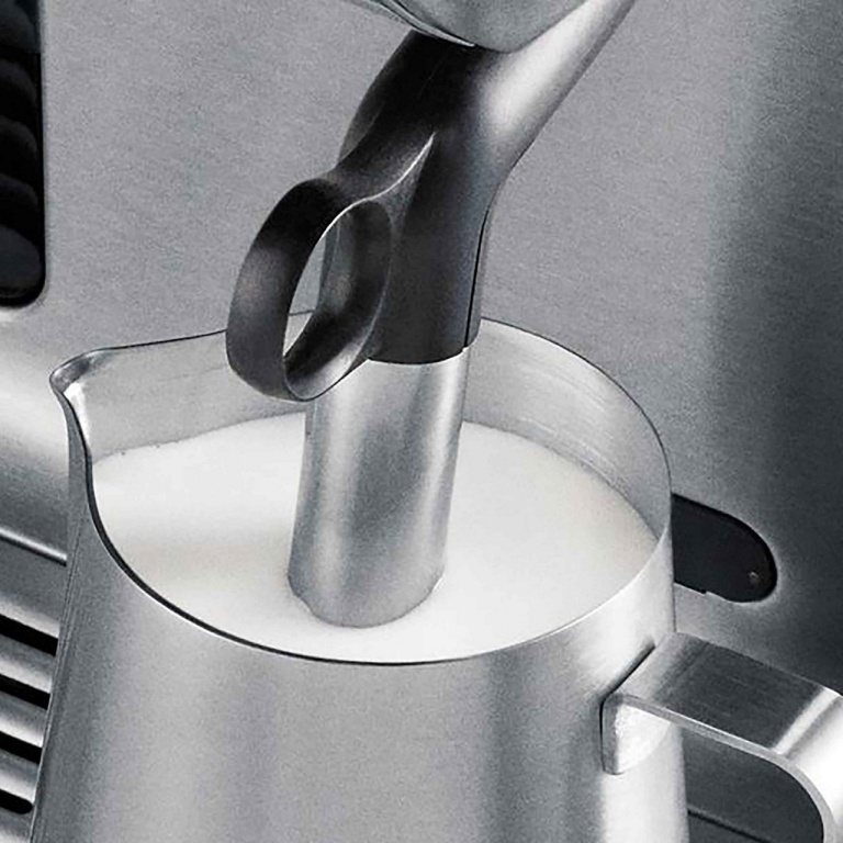 Un dispositivo per montare il latte in metallo è in una brocca di metallo piena di latte bianco schiumato. Il dispositivo ha un manico nero.