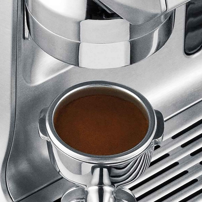 Primo piano di una macchina per caffè espresso in acciaio inossidabile. Un portafiltro è pieno di caffè marrone. Dettagli della macchina visibili.
