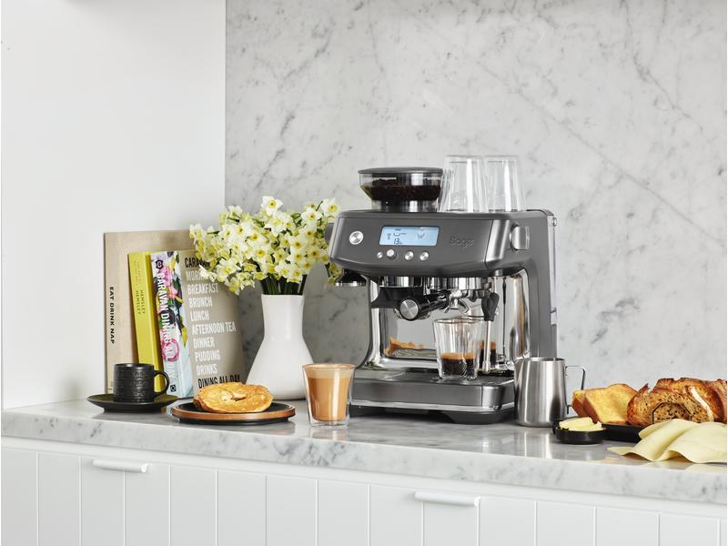 Una macchina da caffè con tazze e un vassoio con pasticcini è su un ripiano della cucina.