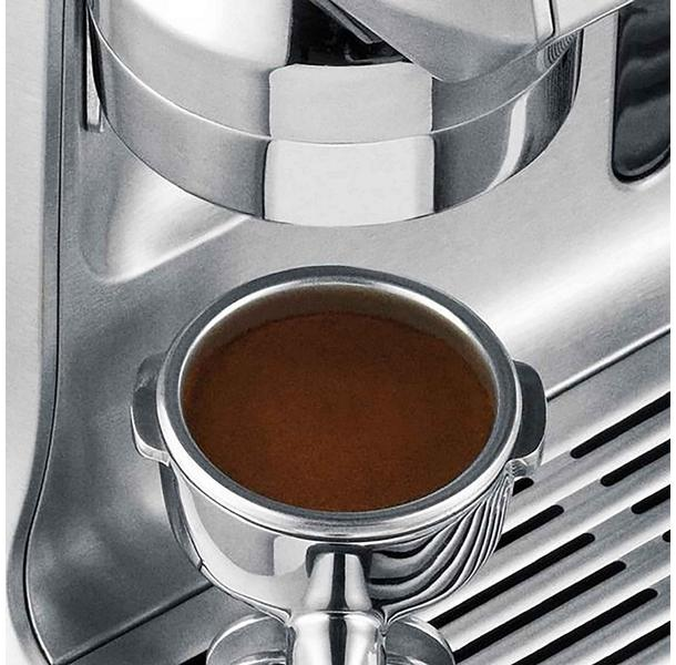 Primo piano del portafiltro di una macchina da caffè pieno di espresso, finitura cromata.