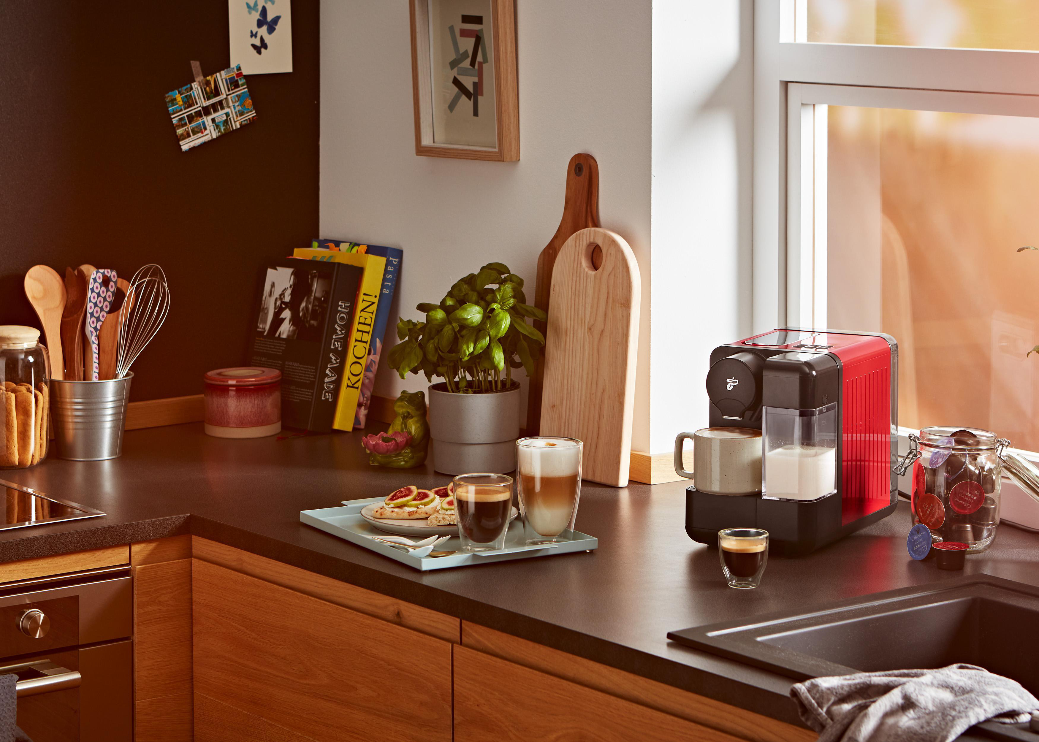 Eine Küchenszene mit einer Kaffeemaschine, Tassen und einem Tablett mit Essen.