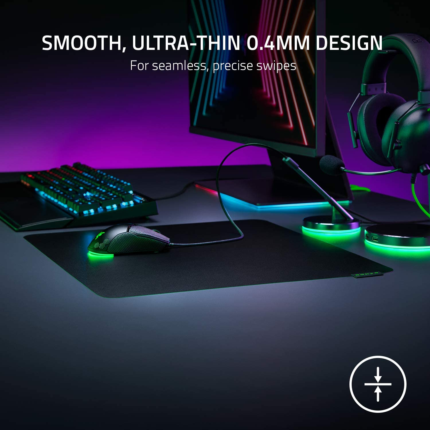 Configuración de juego: ratón en una alfombrilla, teclado, auriculares y monitor en un escritorio. Iluminación morada y verde.