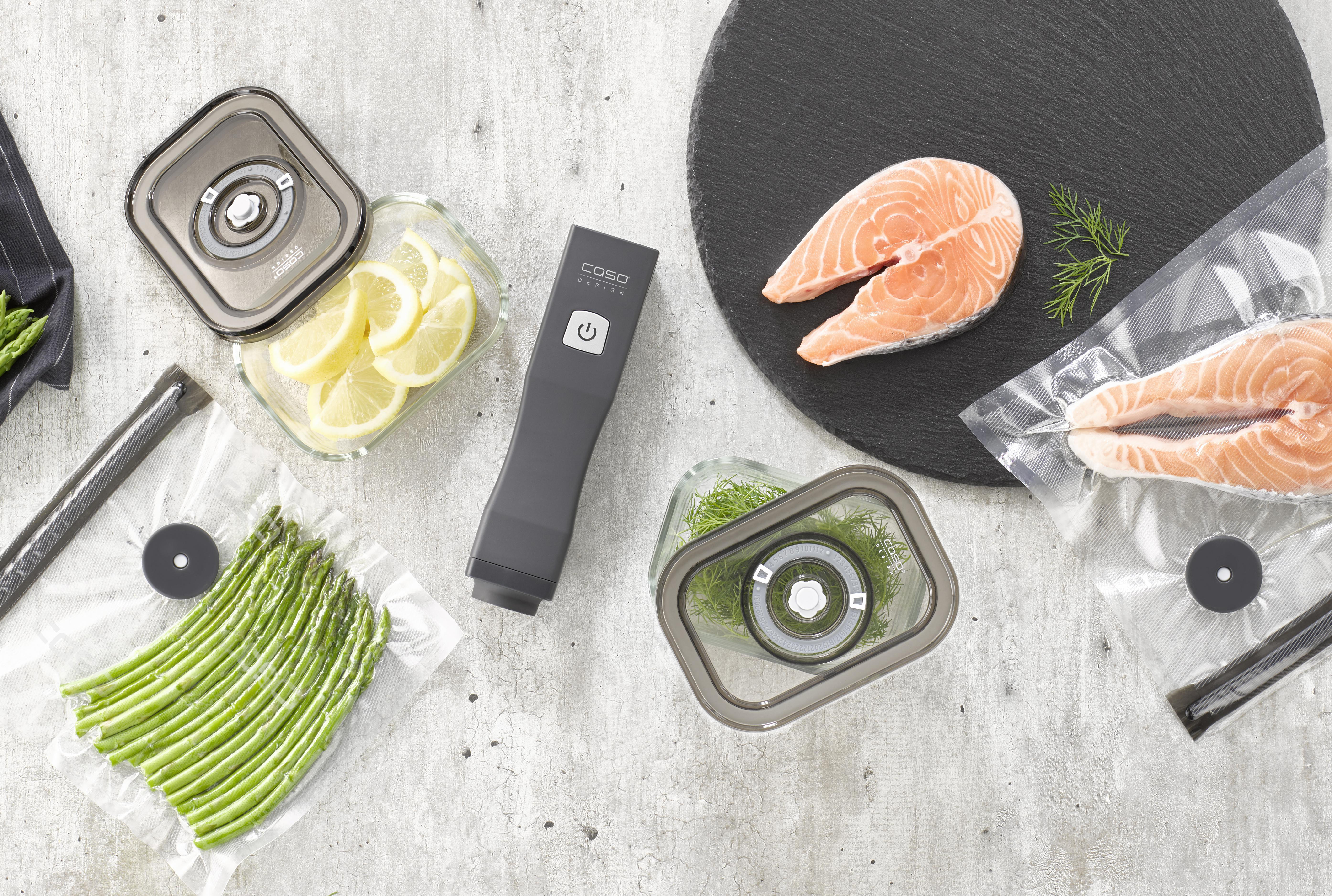 Vakuumiergerät mit Lachs, Spargel und Zitronen auf einer Oberfläche.